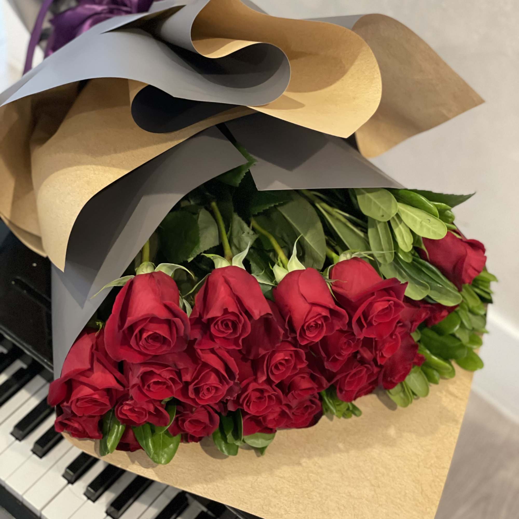 Large wrapped bouquet of red roses resting on piano keys