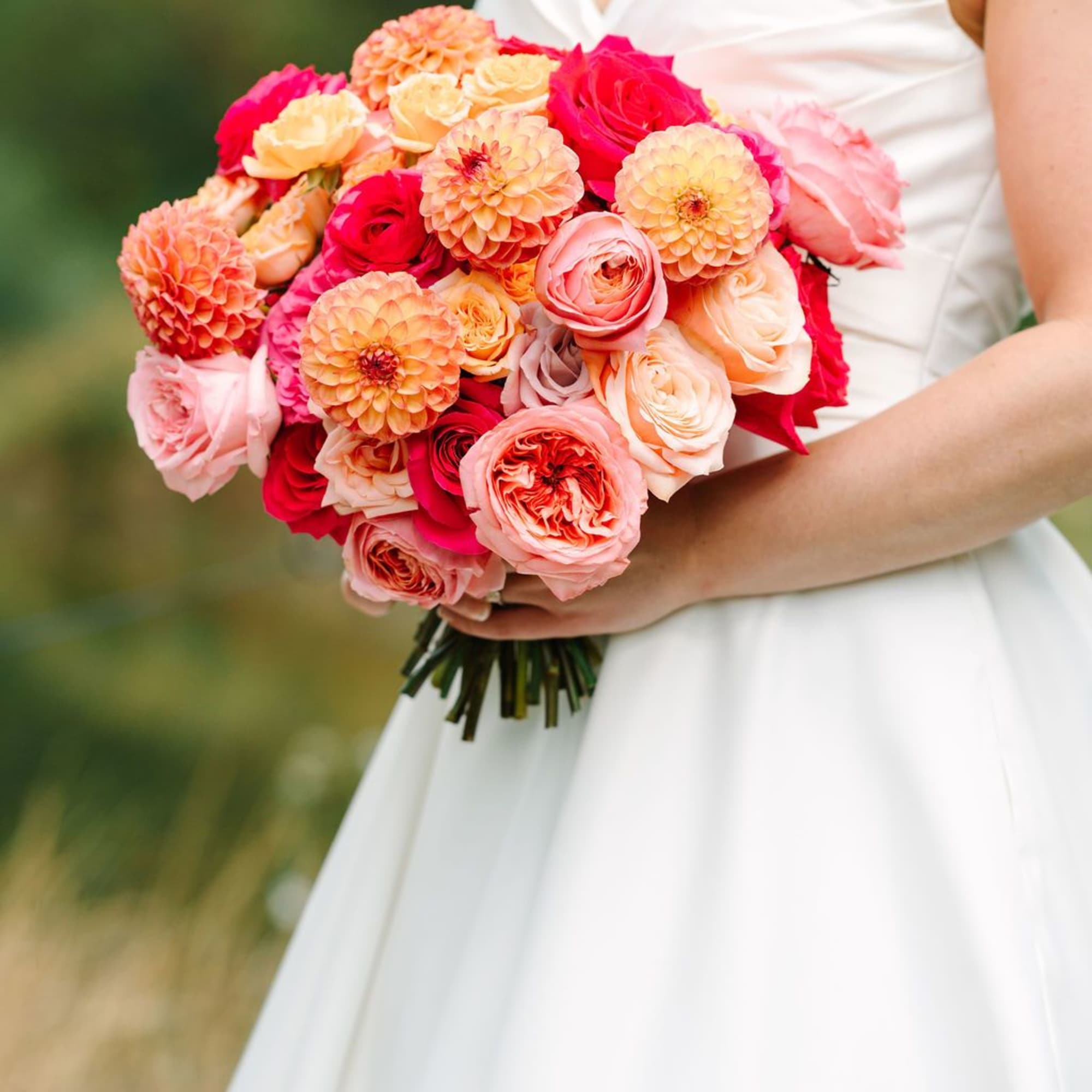 Bride holding a round hand-tied bouquet of pink, peach, and orange roses and dahlias