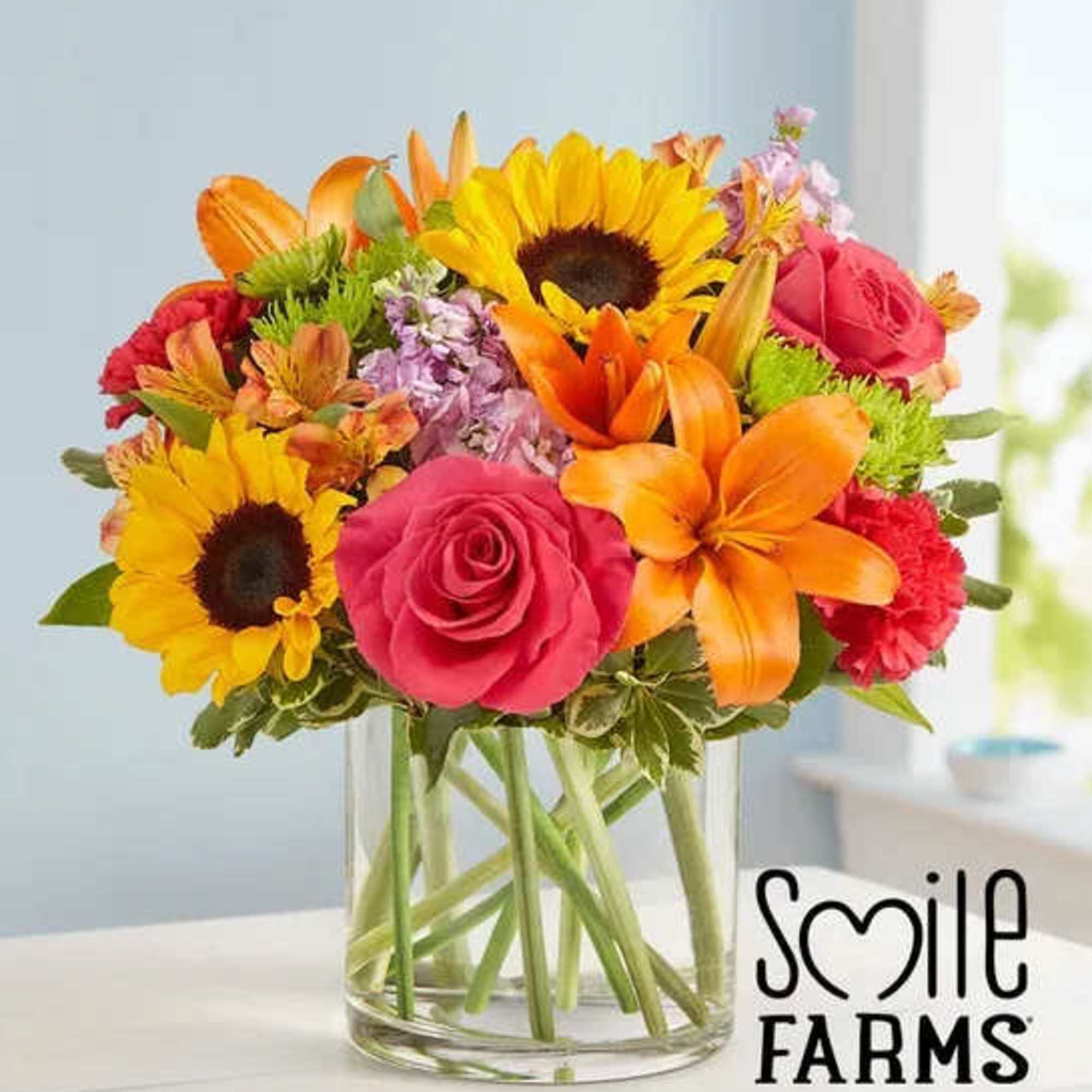 Bright mixed bouquet with sunflowers, orange lilies, and pink roses in a clear glass vase