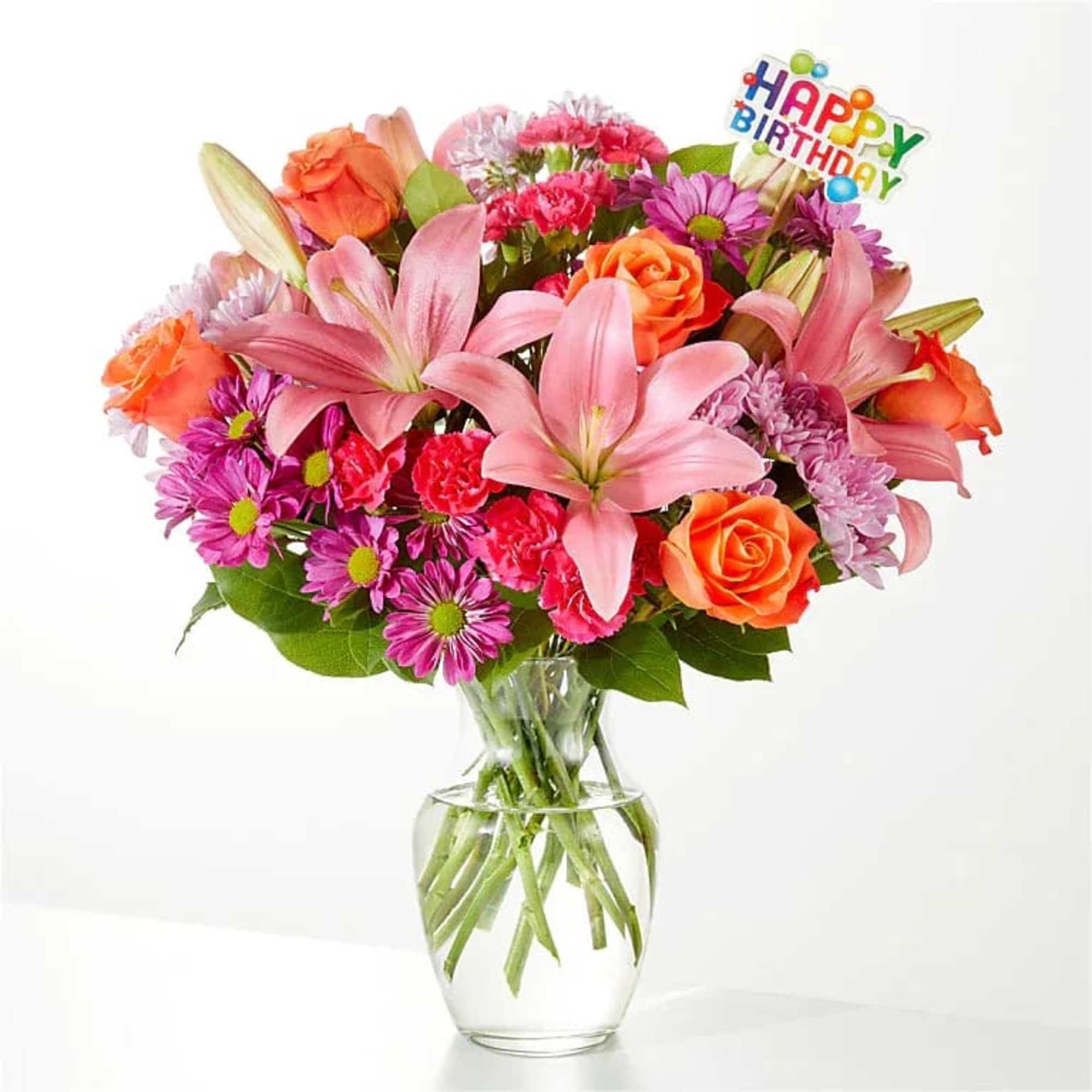 Bright bouquet of pink lilies, orange roses, and purple daisies in a clear glass vase with Happy Birthday pick