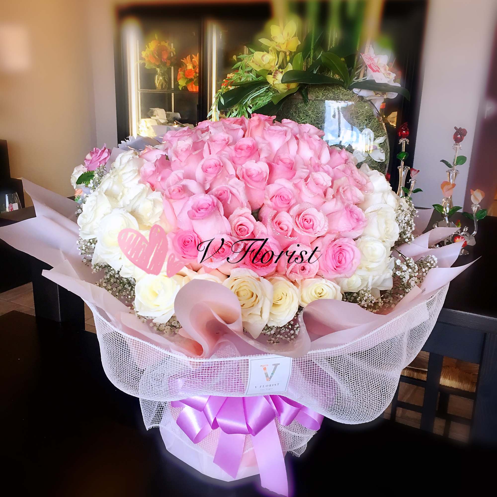 Large round arrangement of pink and white roses in a pink hatbox with decorative wrap and ribbon.