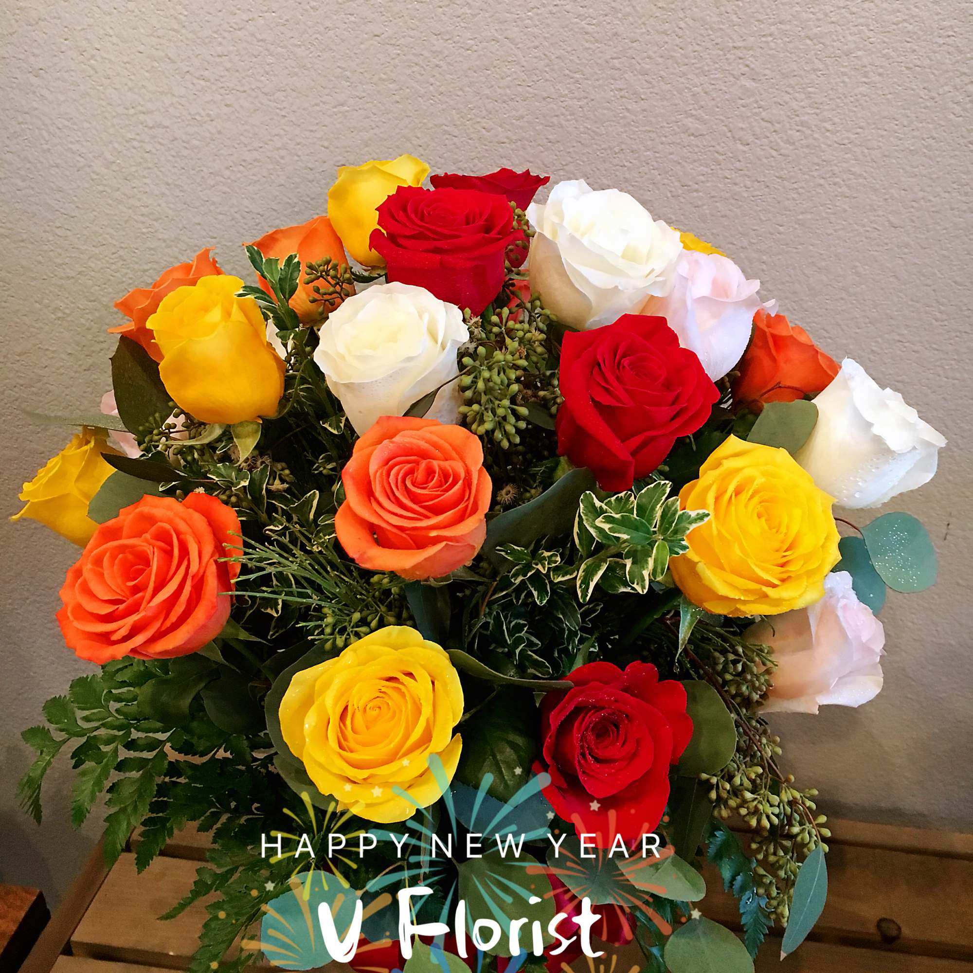 Arrangement of red, yellow, orange, and white roses with greenery on a wooden surface