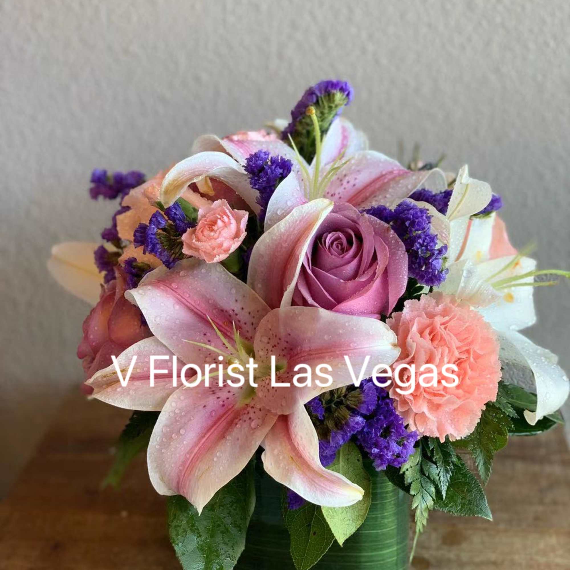 Compact arrangement of pink lilies, lavender roses, and peach carnations in a green cube vase