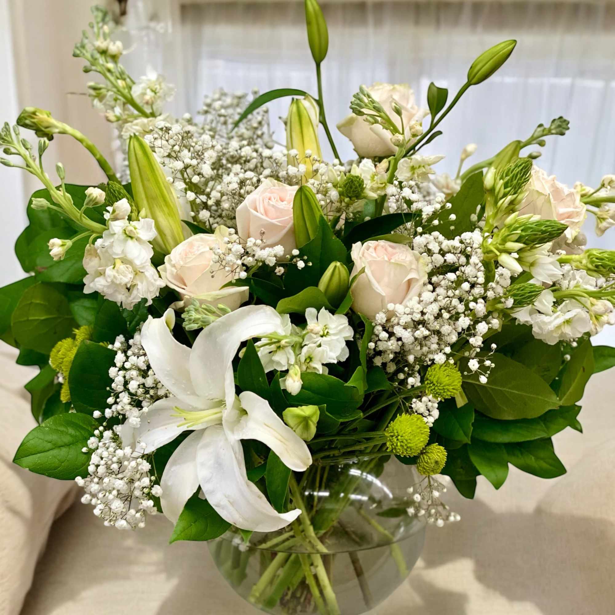 A mixed arrangement of white lilies, blush roses, green button, white filler