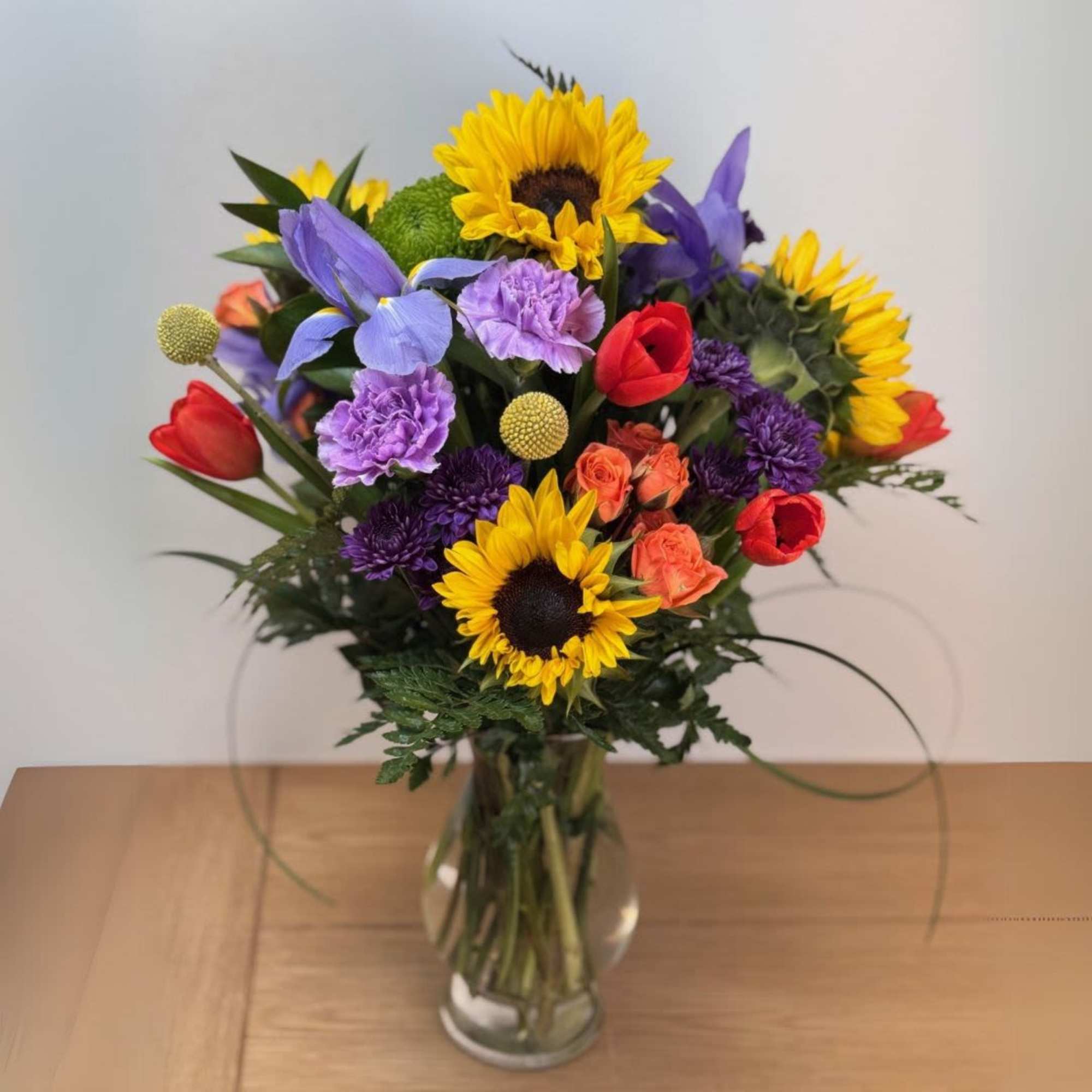 Bright mixed bouquet of sunflowers, tulips, irises, and other blooms in a clear glass vase