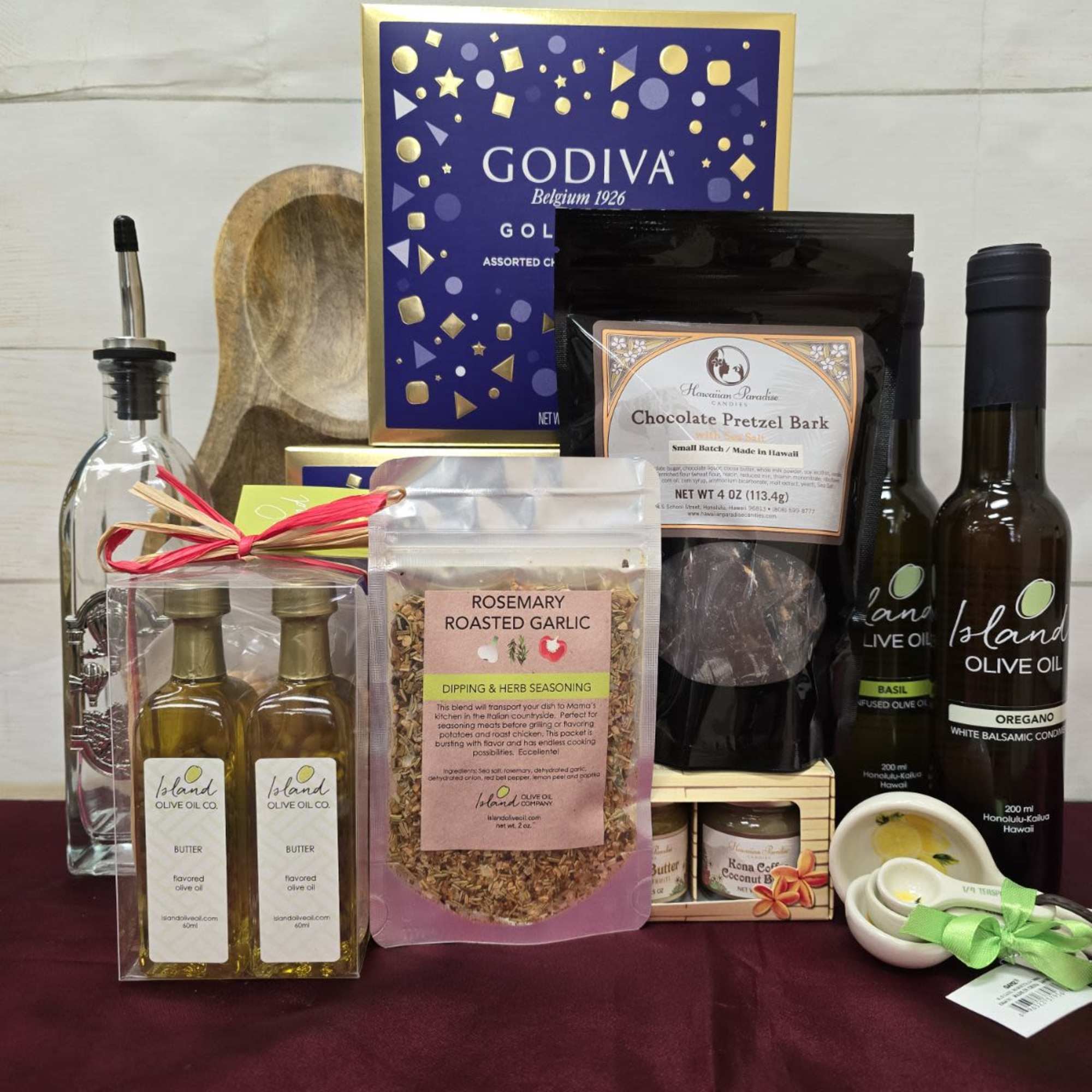 Gourmet gift set with Godiva chocolates, olive oils, seasonings, and snacks on a burgundy cloth.