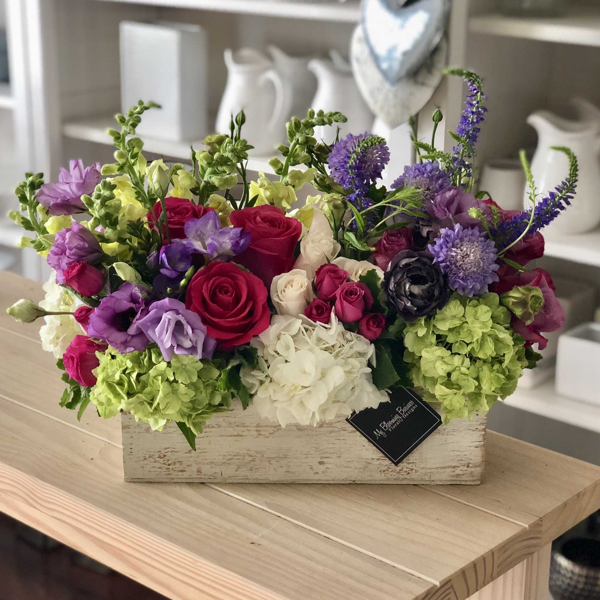 Mixed bouquet of roses, hydrangeas, and purple blooms in a wooden box