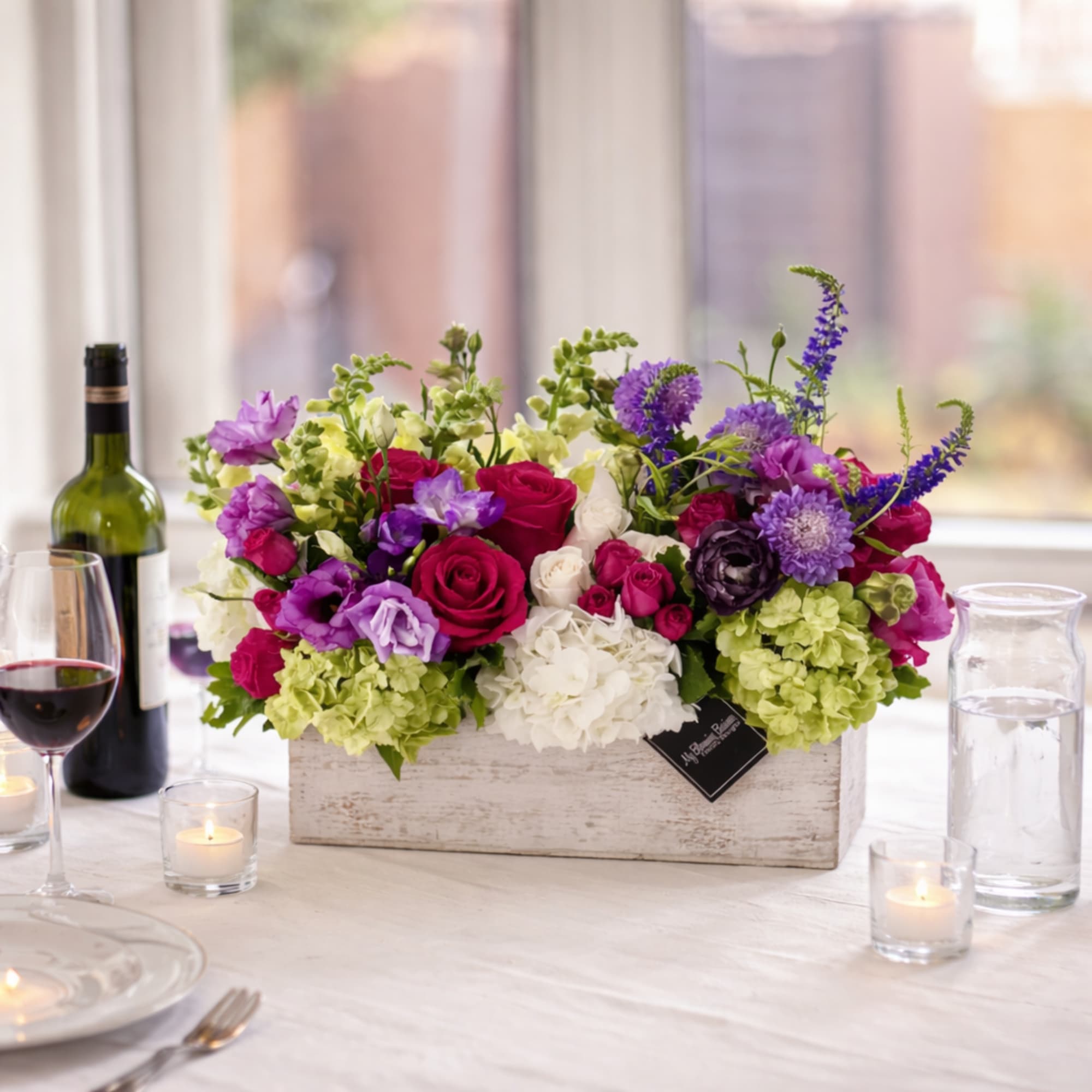 Mixed bouquet in a white wooden box with candles and wine on a table
