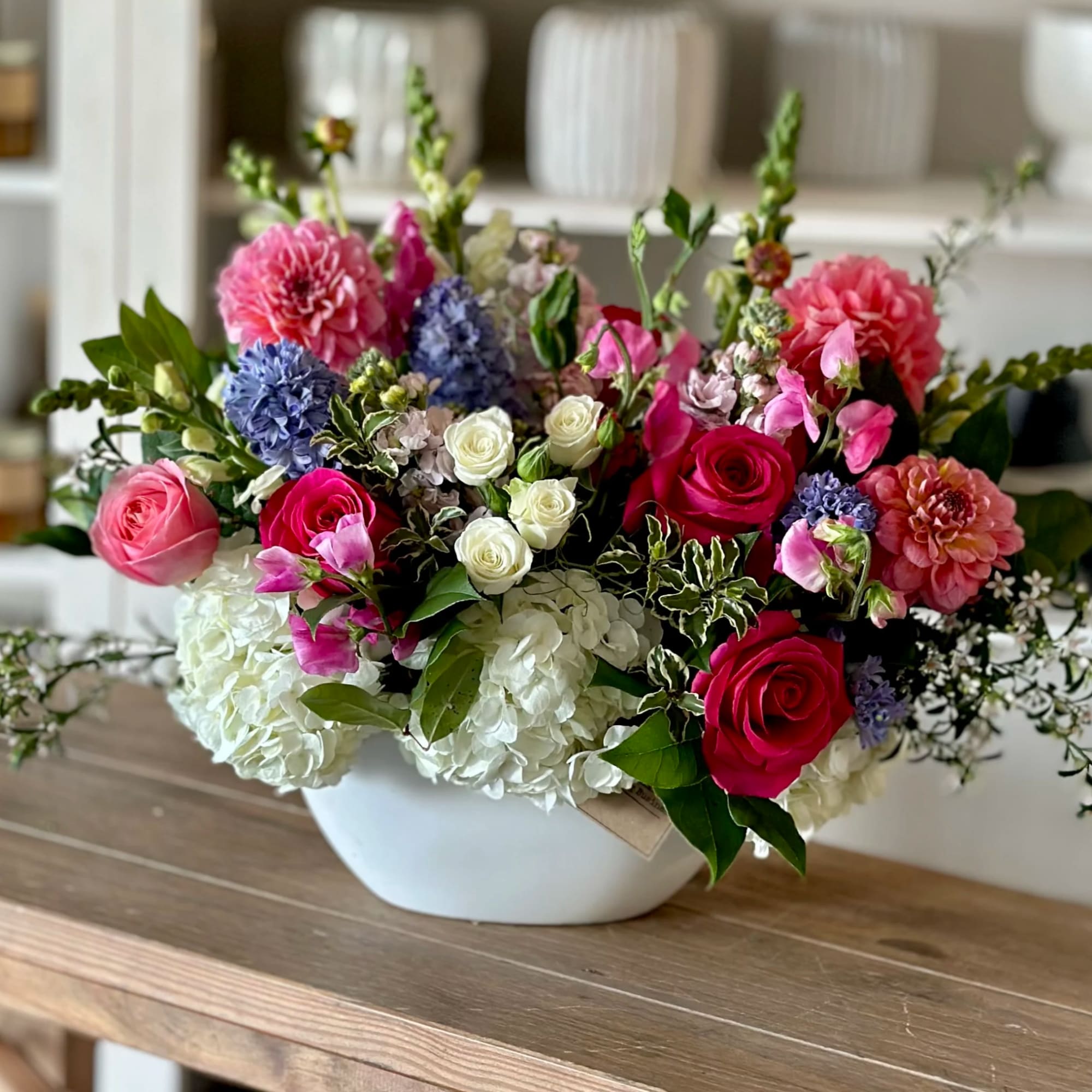 Mixed bouquet of pink, white, and blue flowers in a white bowl vase
