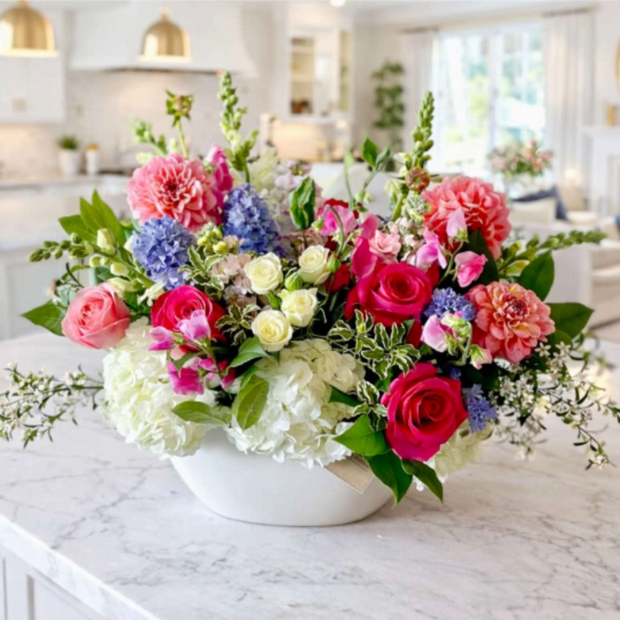 Mixed bouquet of pink, white, blue, and coral flowers in a white bowl vase