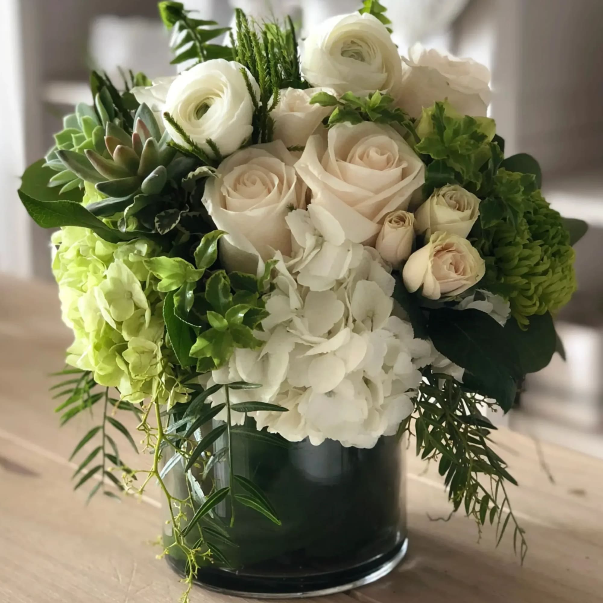 White roses and hydrangeas arranged in a dark glass vase with green succulents.