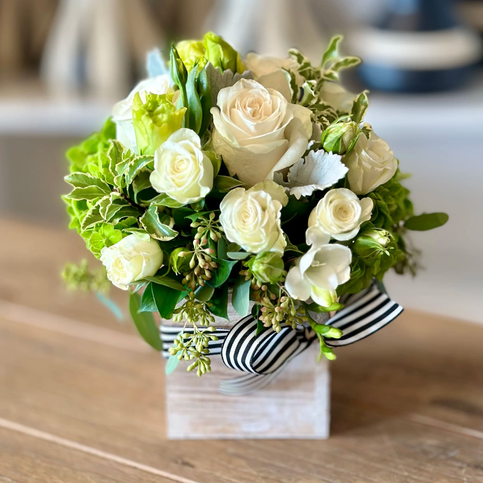 White roses and green blooms arranged in a square box with a striped ribbon