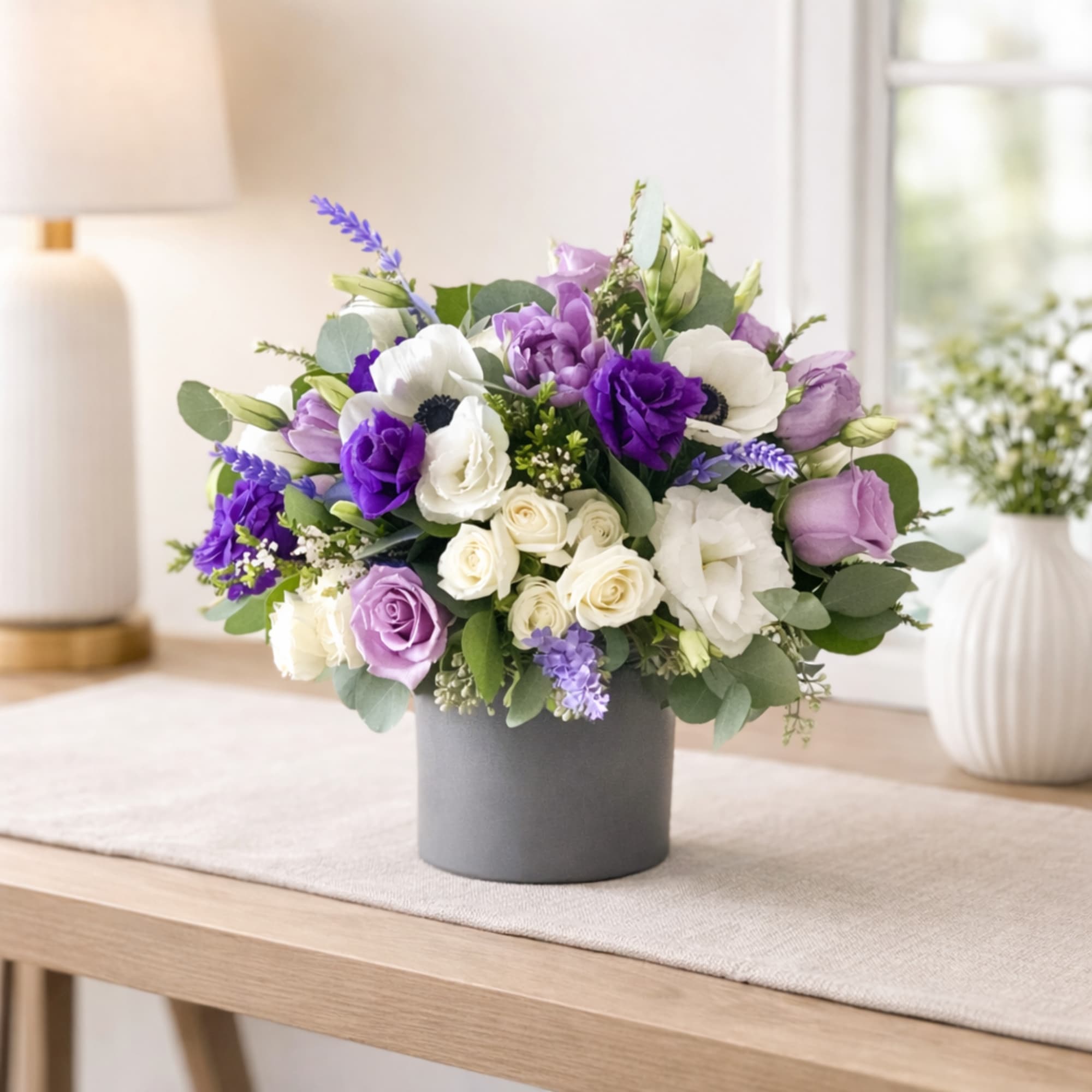 Purple and white bouquet in a gray hatbox-style container