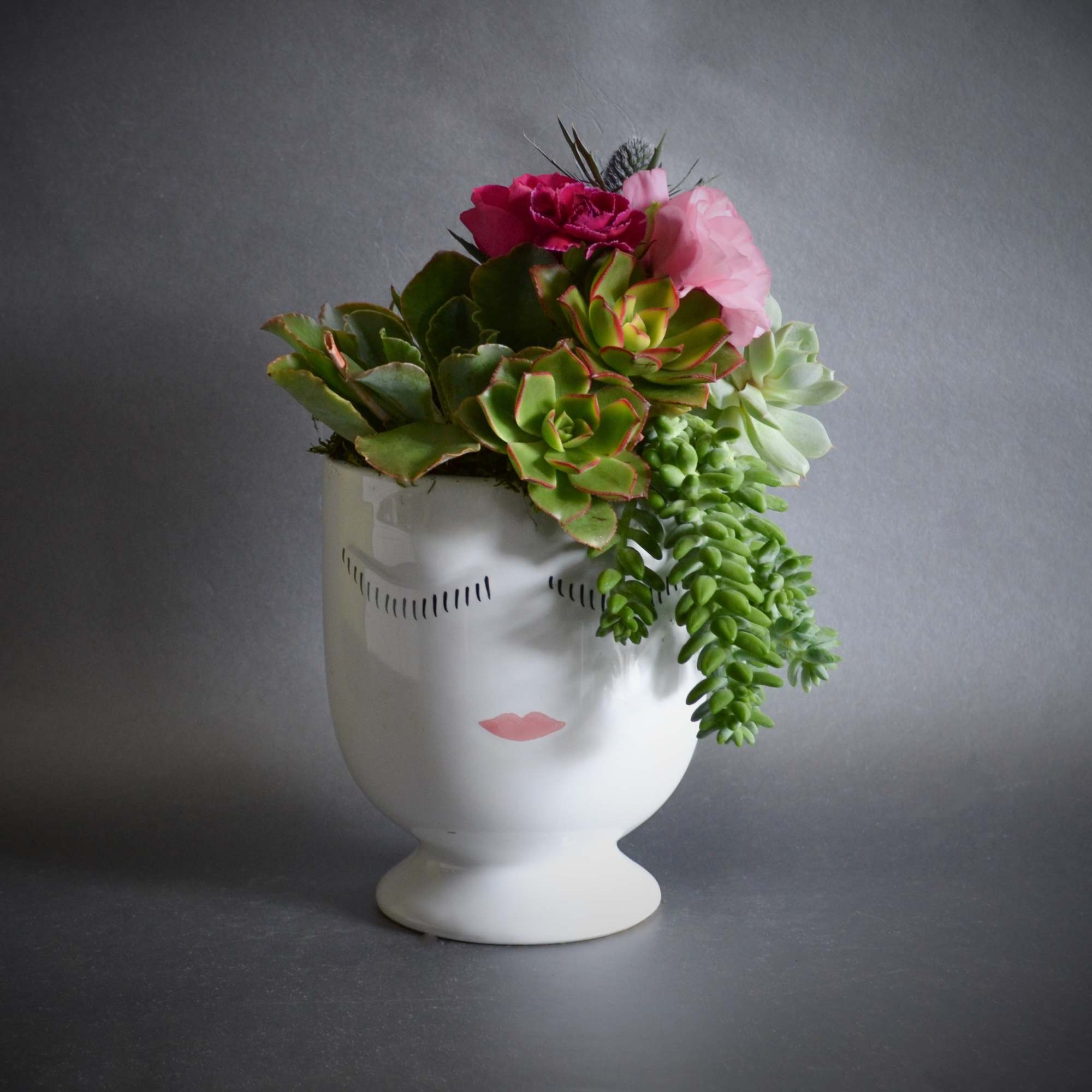 Succulent arrangement in a white face-shaped vase with pink flowers