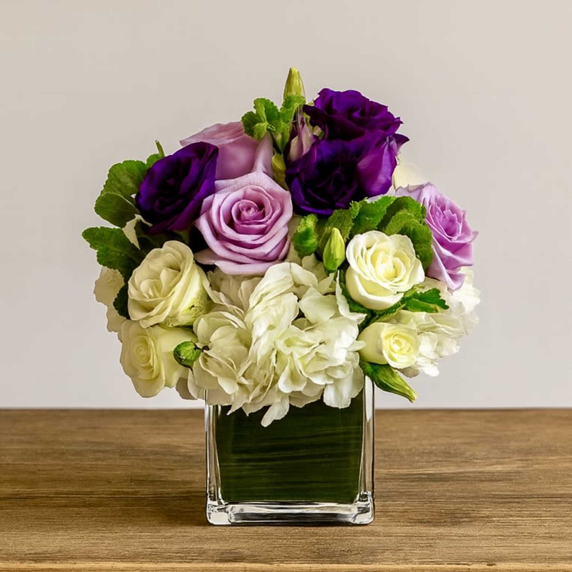 Purple, lavender, and white roses in a clear square vase