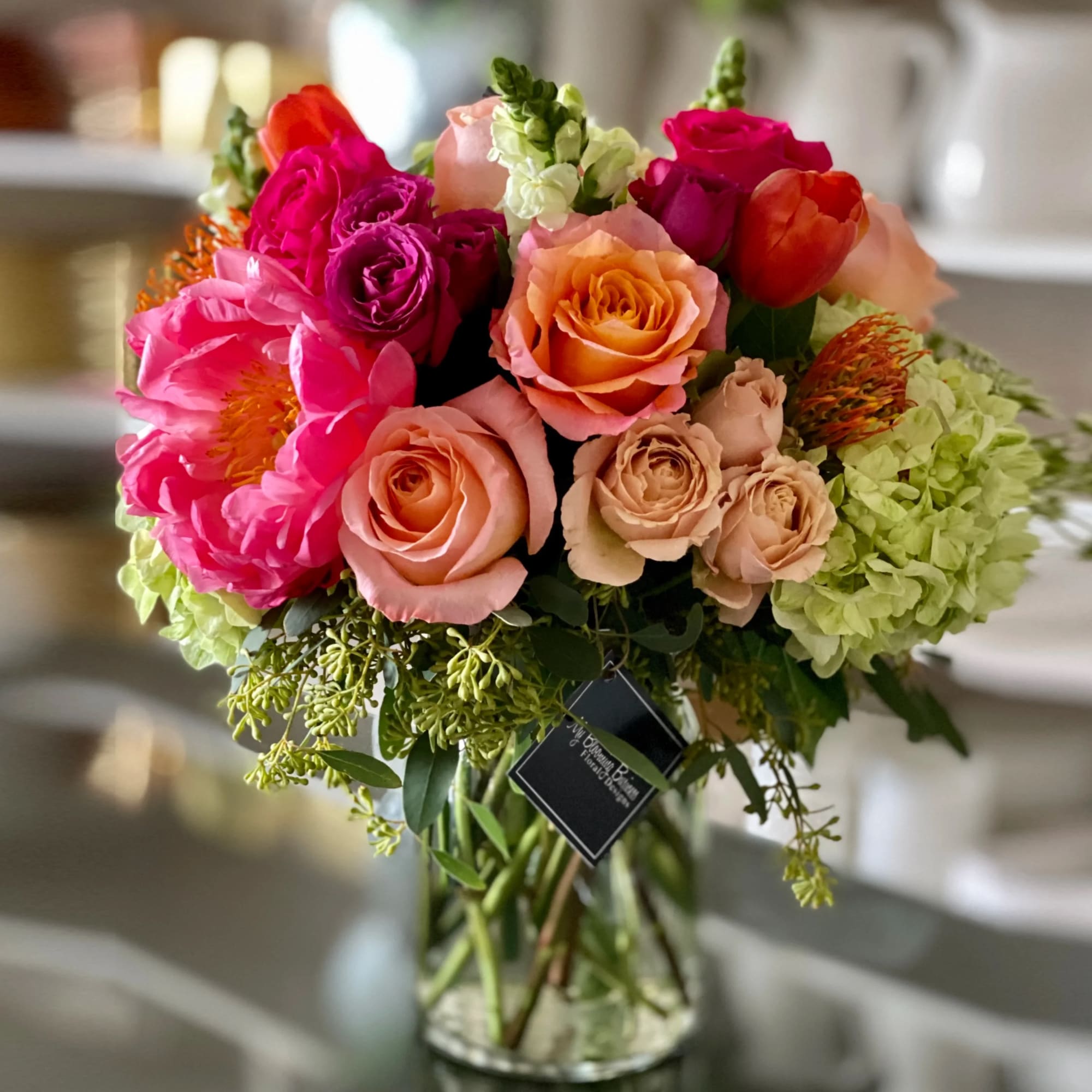 Mixed bouquet of pink, peach, and orange roses in a glass vase