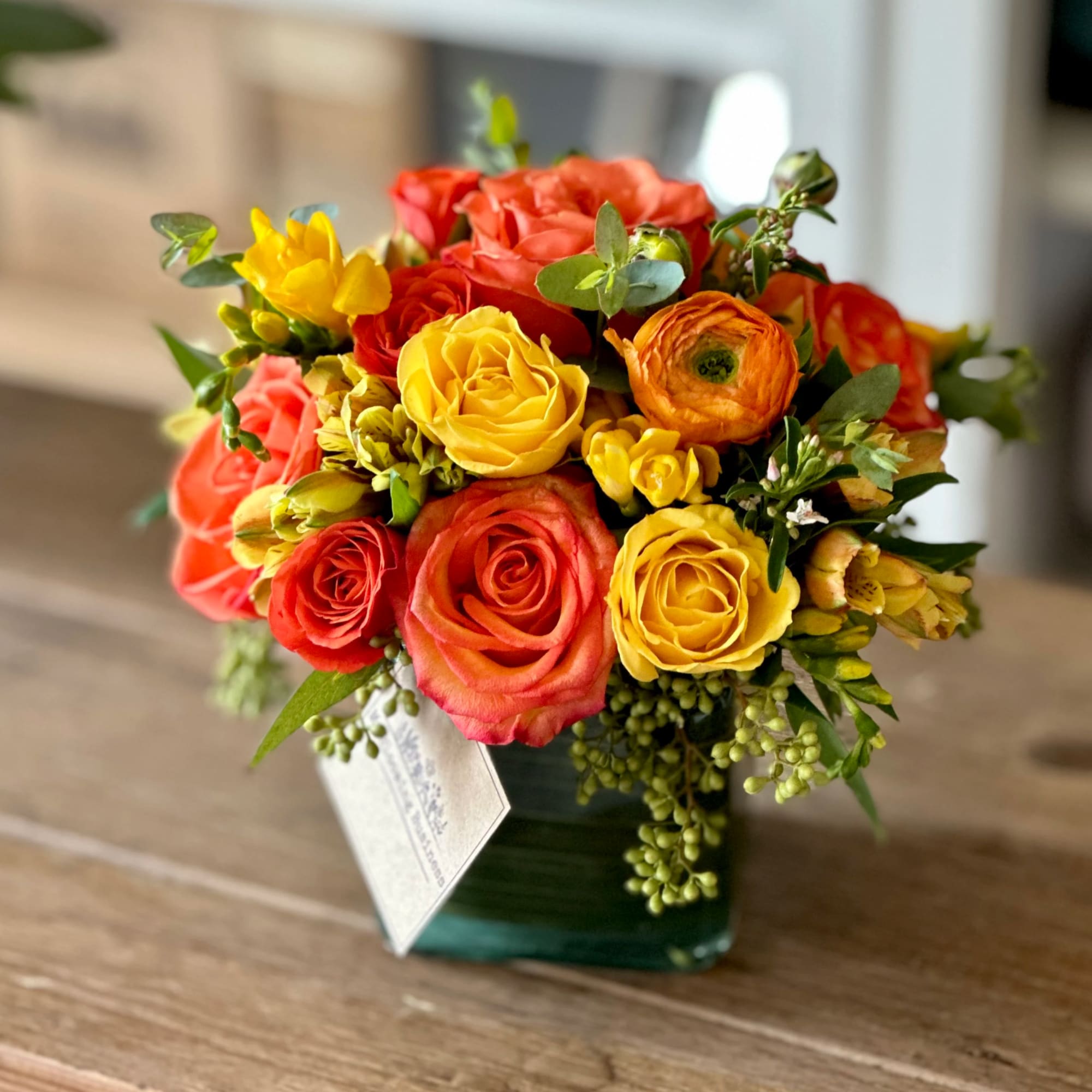 Bouquet of red, yellow, and orange roses in a square glass vase