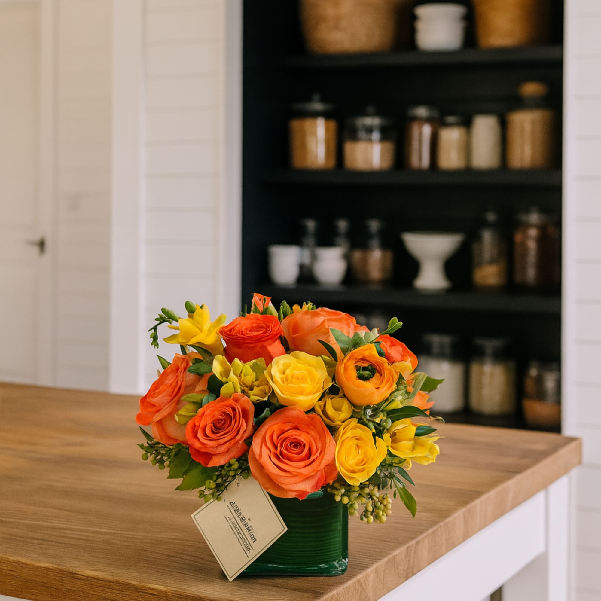 Orange and yellow rose bouquet in a green vase on a kitchen counter