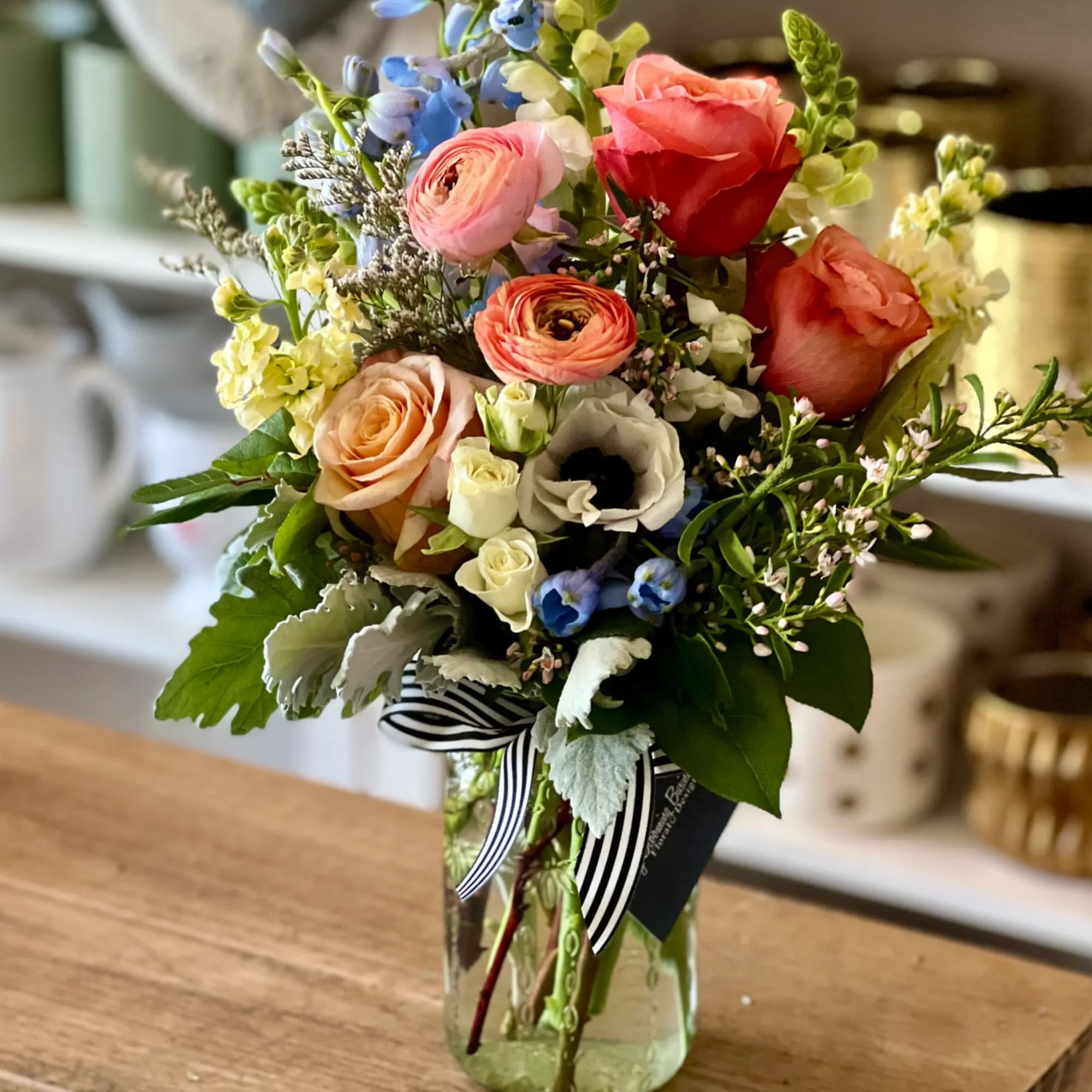 Mixed bouquet of roses, ranunculus, and blue flowers in a glass vase
