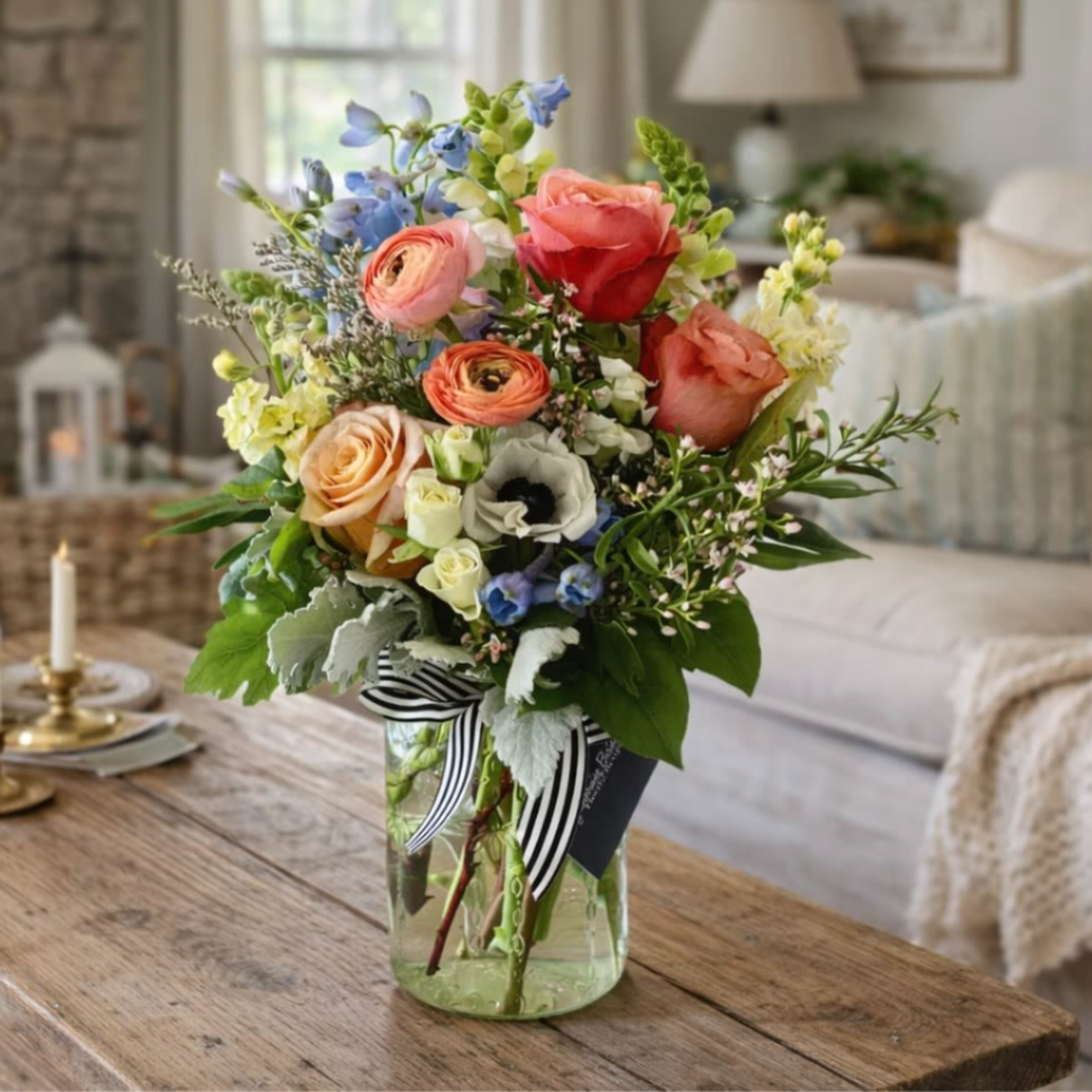 Mixed bouquet of roses, ranunculus, and blue flowers in a glass vase