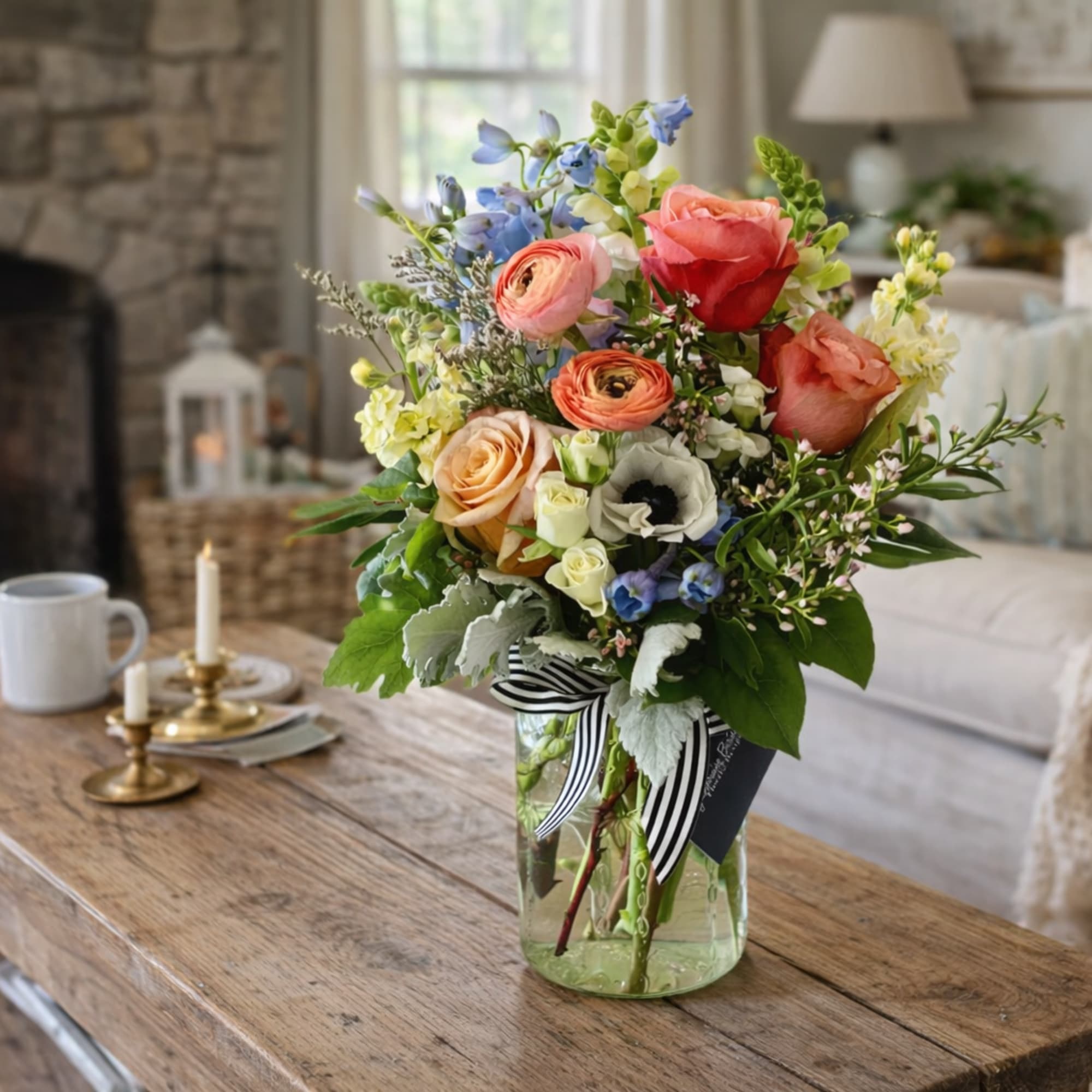 Mixed bouquet of roses, ranunculus, and blue flowers in a glass vase