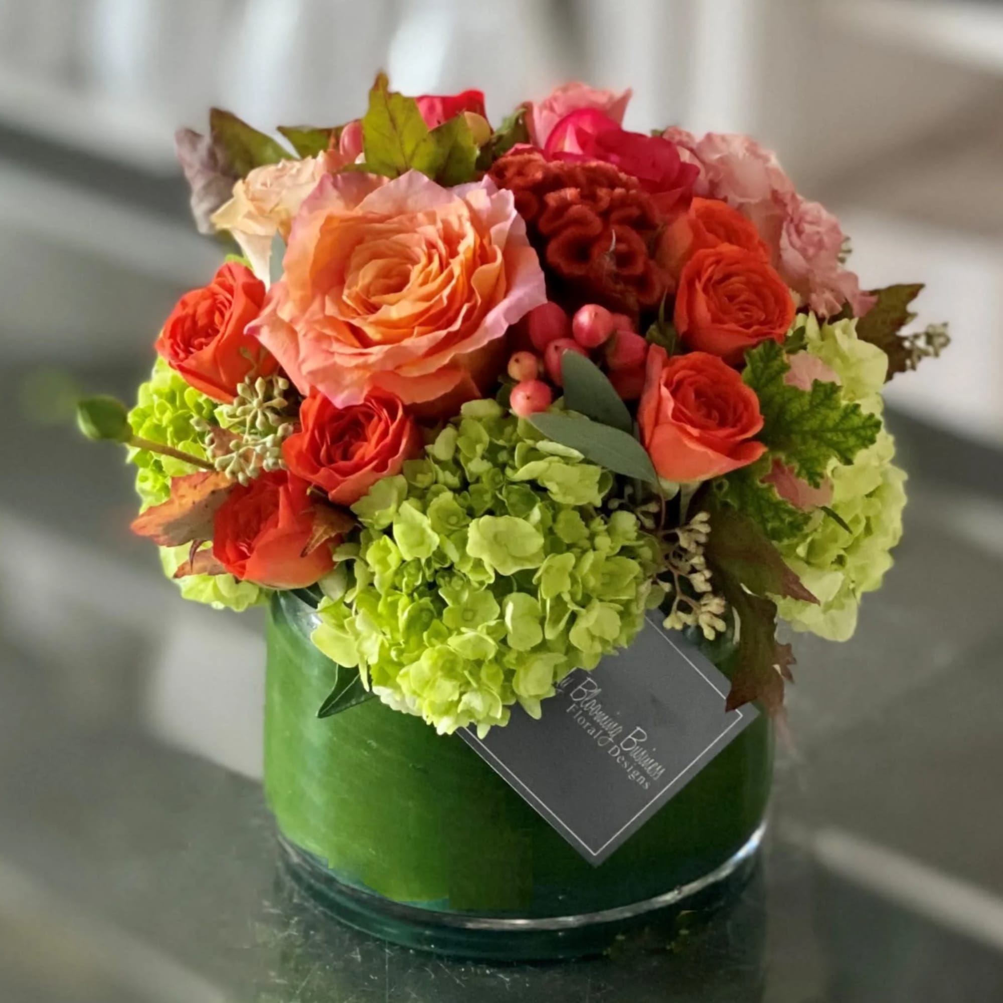 Orange and pink roses with green hydrangeas in a glass vase