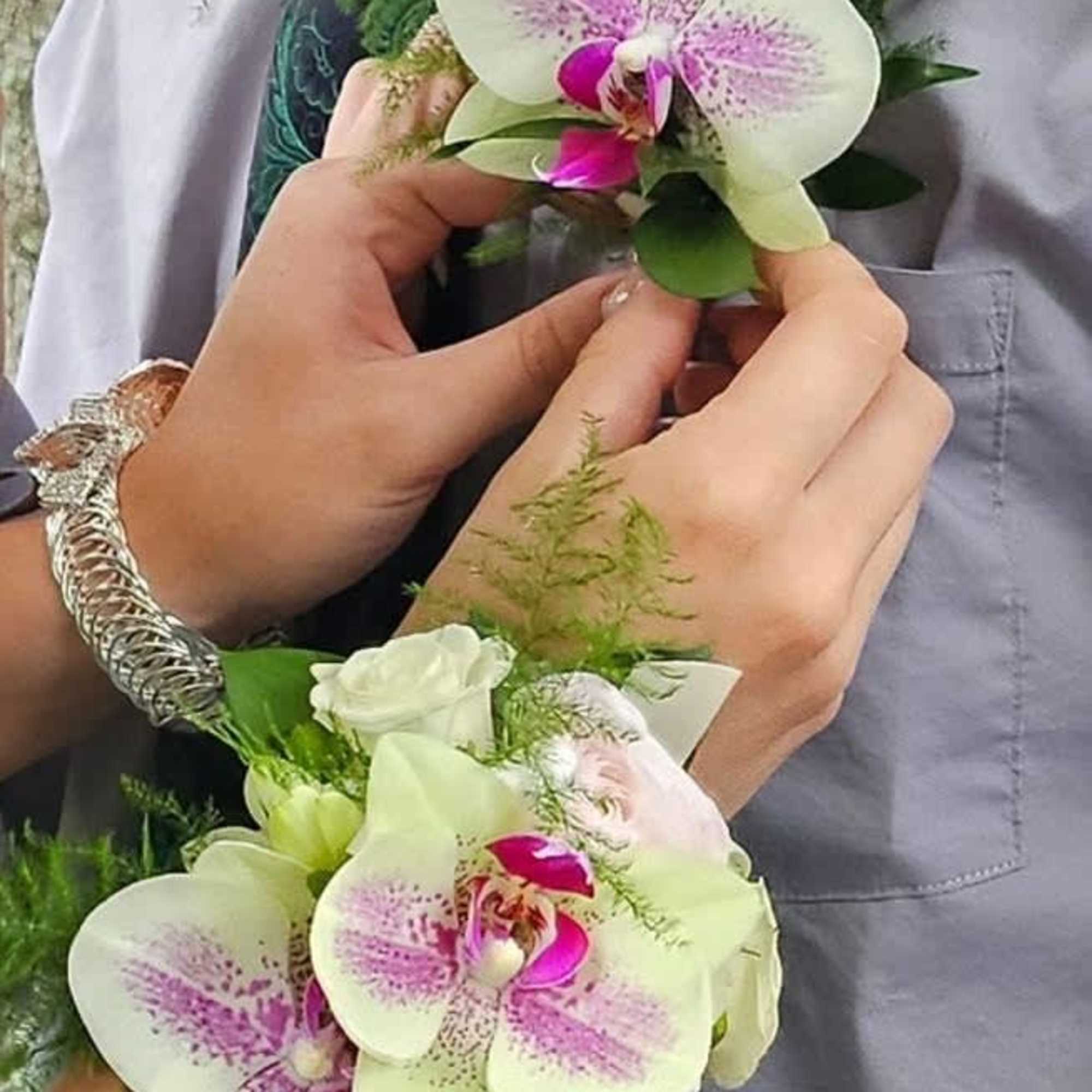Two orchid corsages with white and pink blooms being held in hands