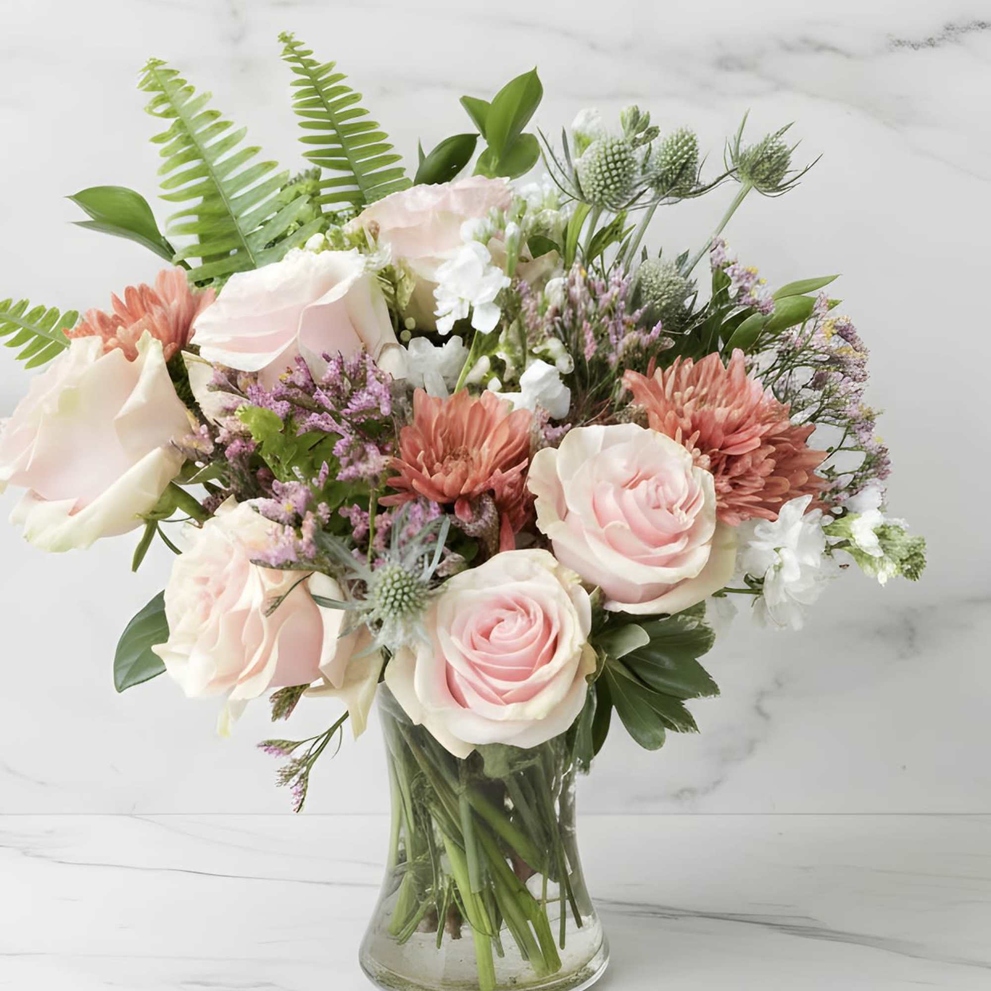 Pink and white roses with coral mums in a glass vase