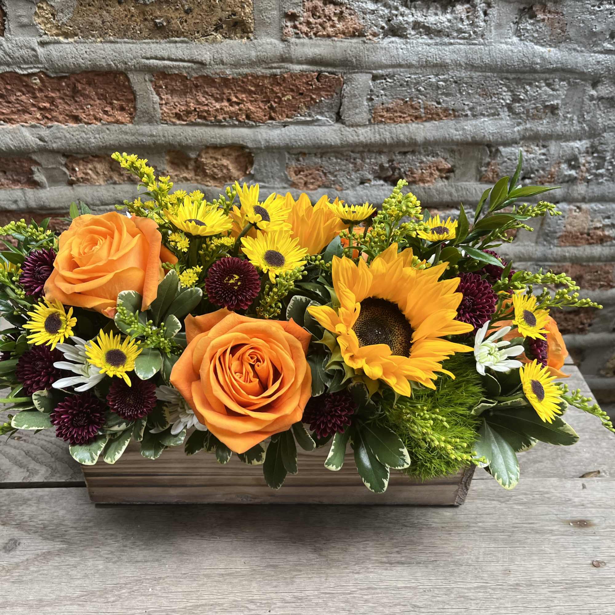 Orange roses and sunflowers in a rectangular wooden planter