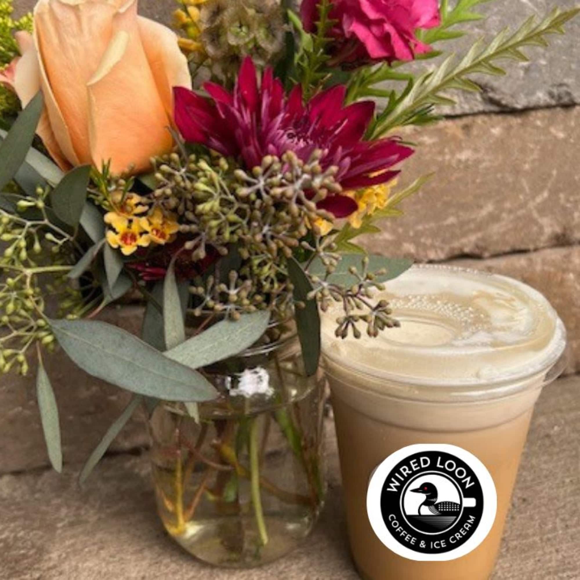 Bouquet of peach and magenta flowers in a glass vase beside a lidded iced drink