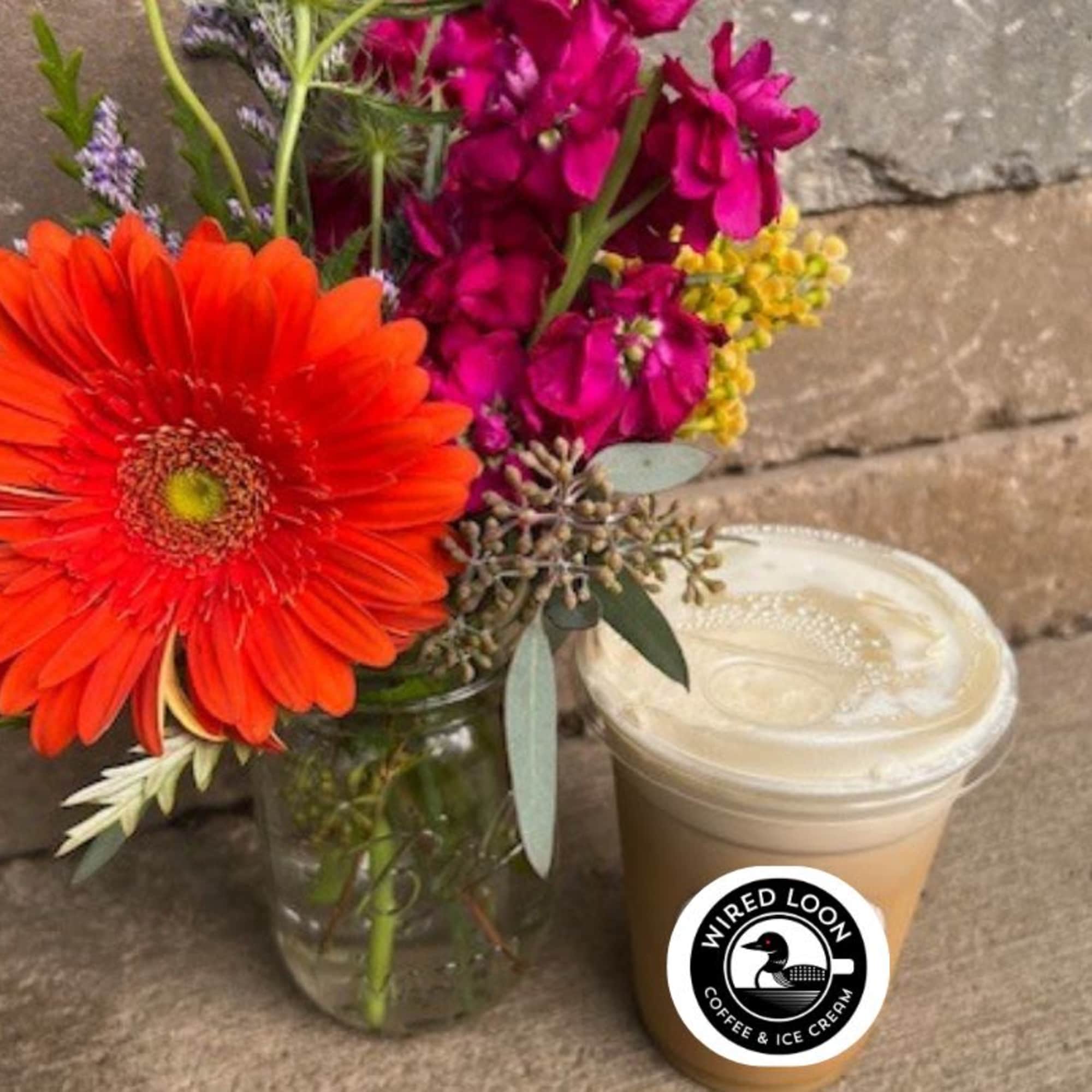Bright mixed bouquet in a glass jar beside a lidded iced coffee cup