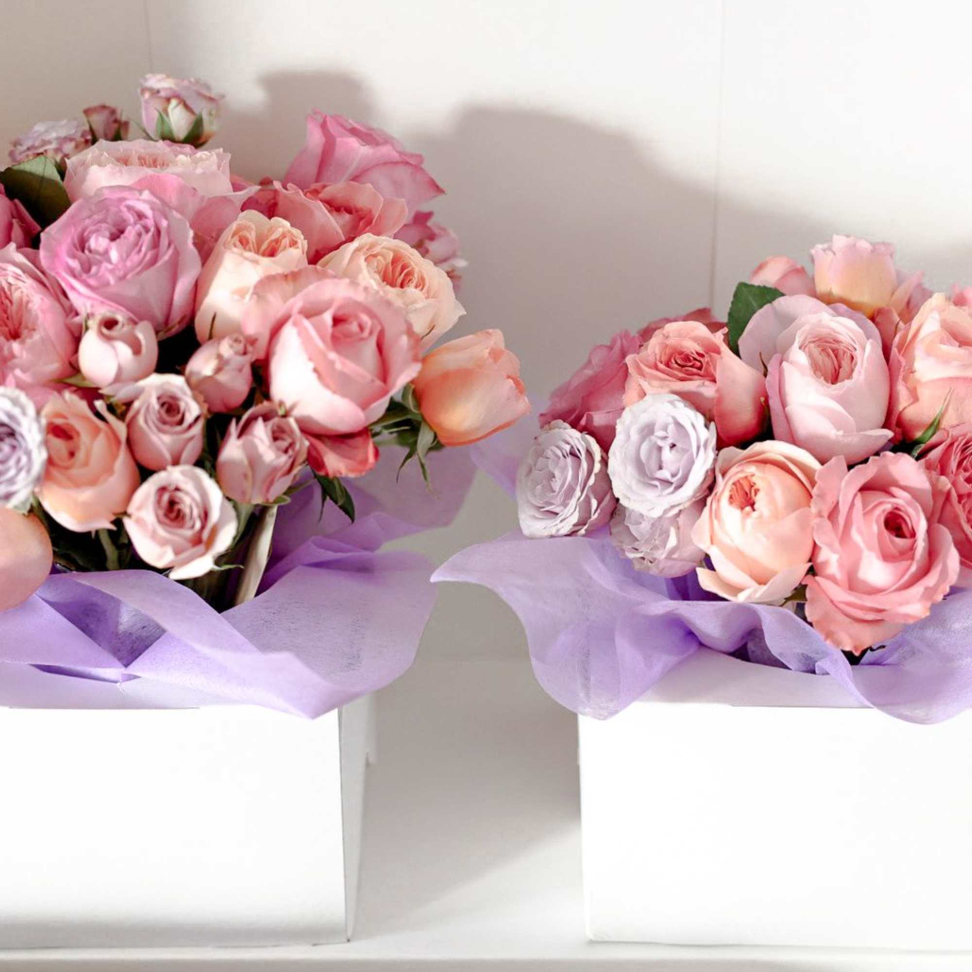 Two pink rose bouquets in white boxes with lavender wrapping
