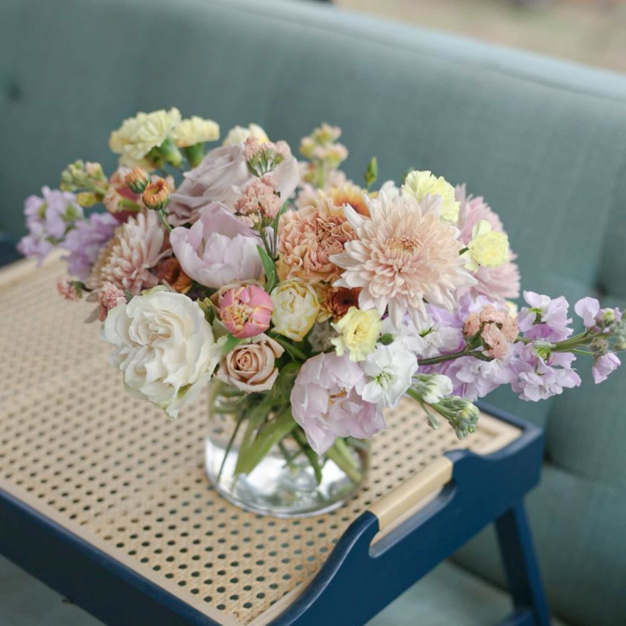 Pastel mixed bouquet in a clear glass vase on a woven tray