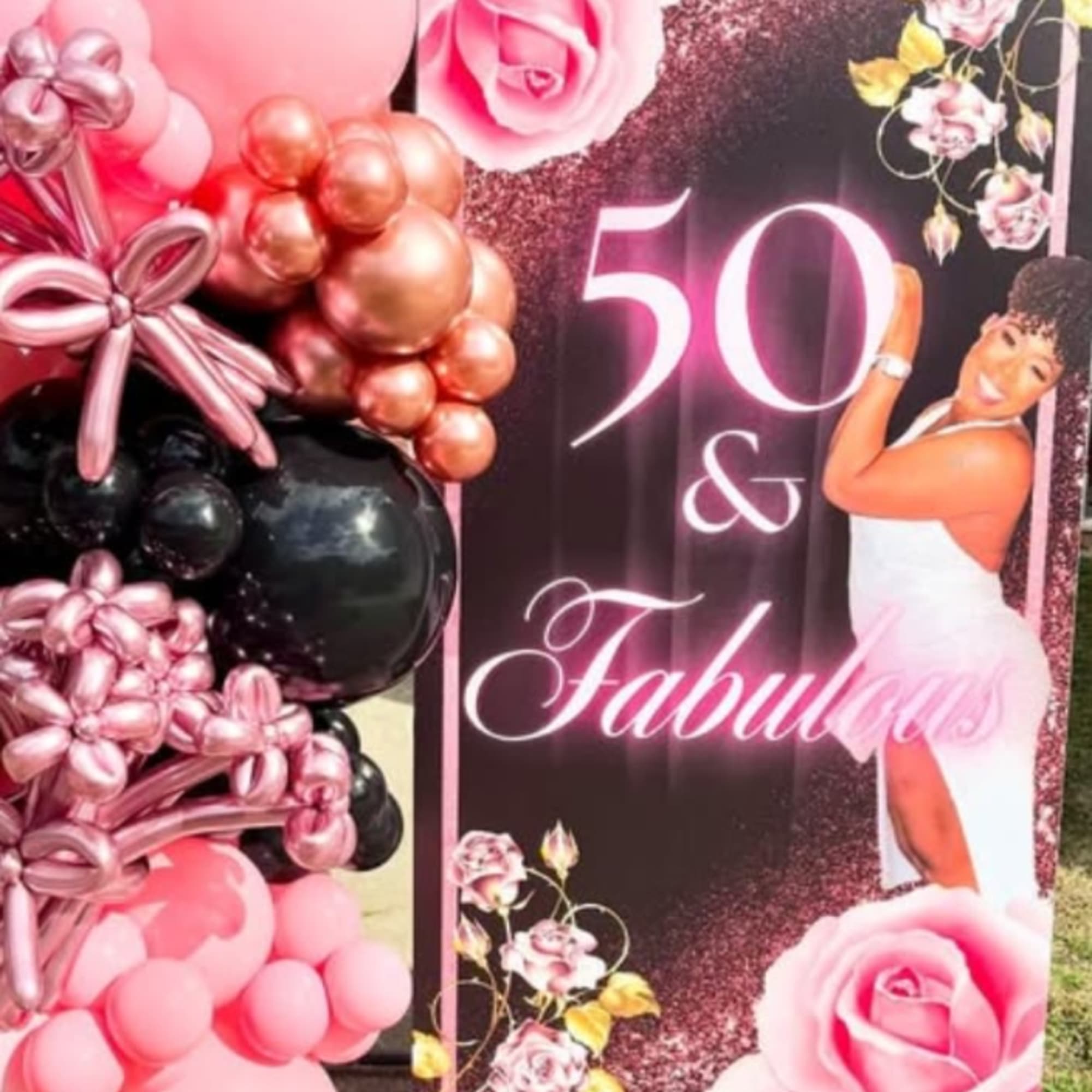 Pink and black balloon display beside a "50 & Fabulous" party sign