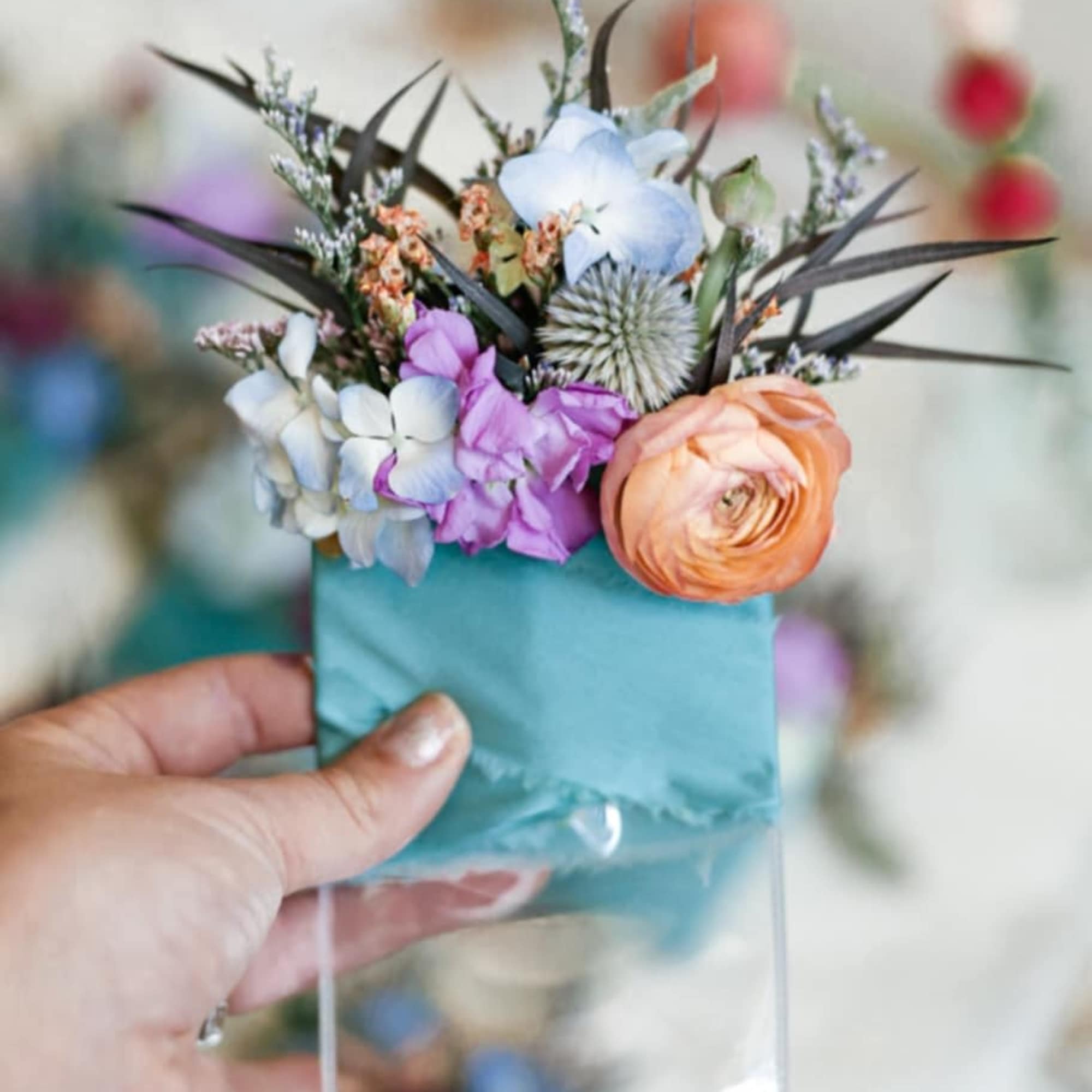 Small floral arrangement in a clear holder with peach, purple, and white blooms