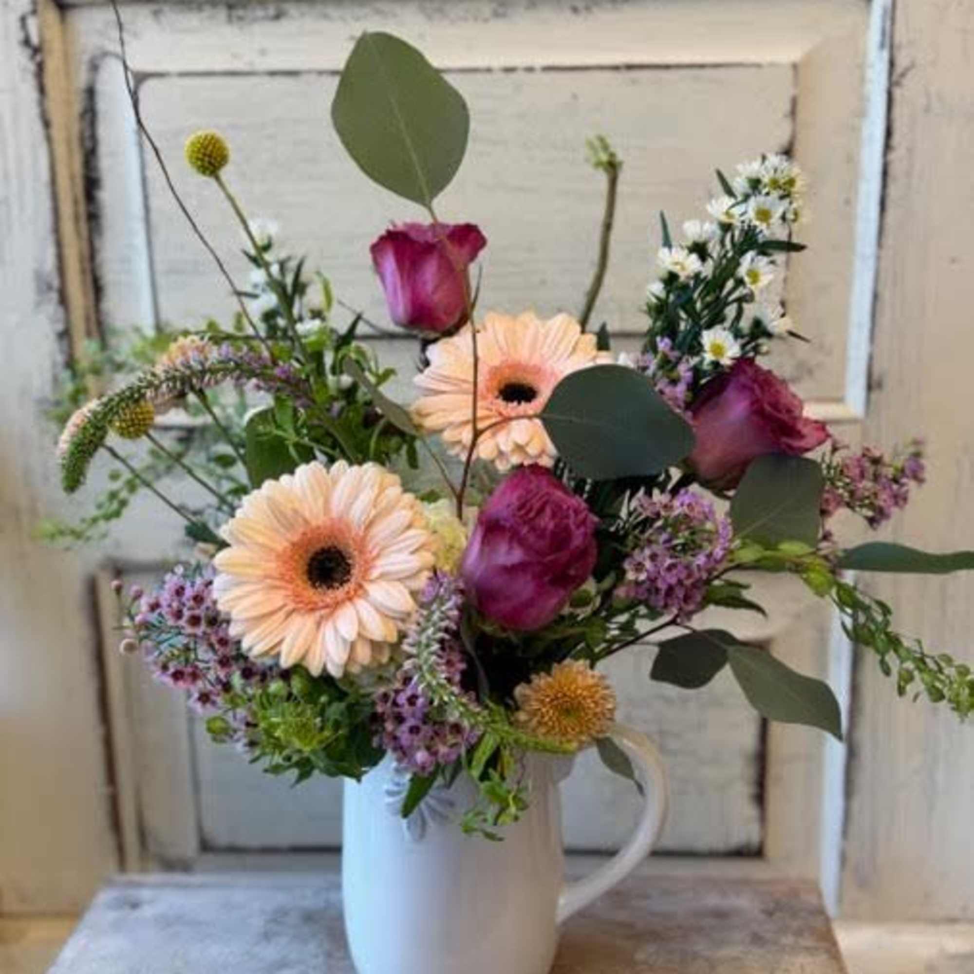 A charming arrangement of seasonal flowers, fillers and foliage in a ceramic