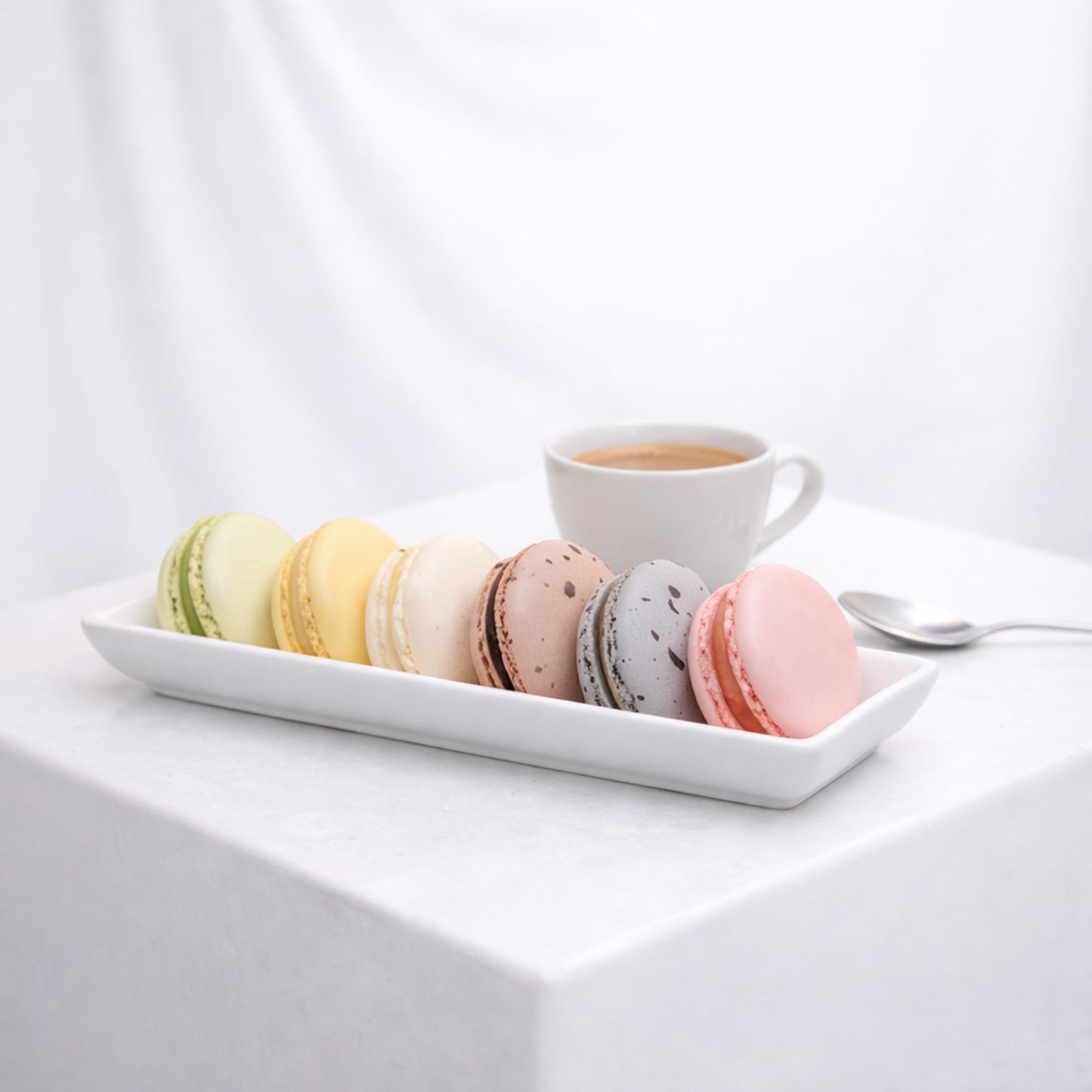 Tray of pastel macarons with a cup of coffee and spoon