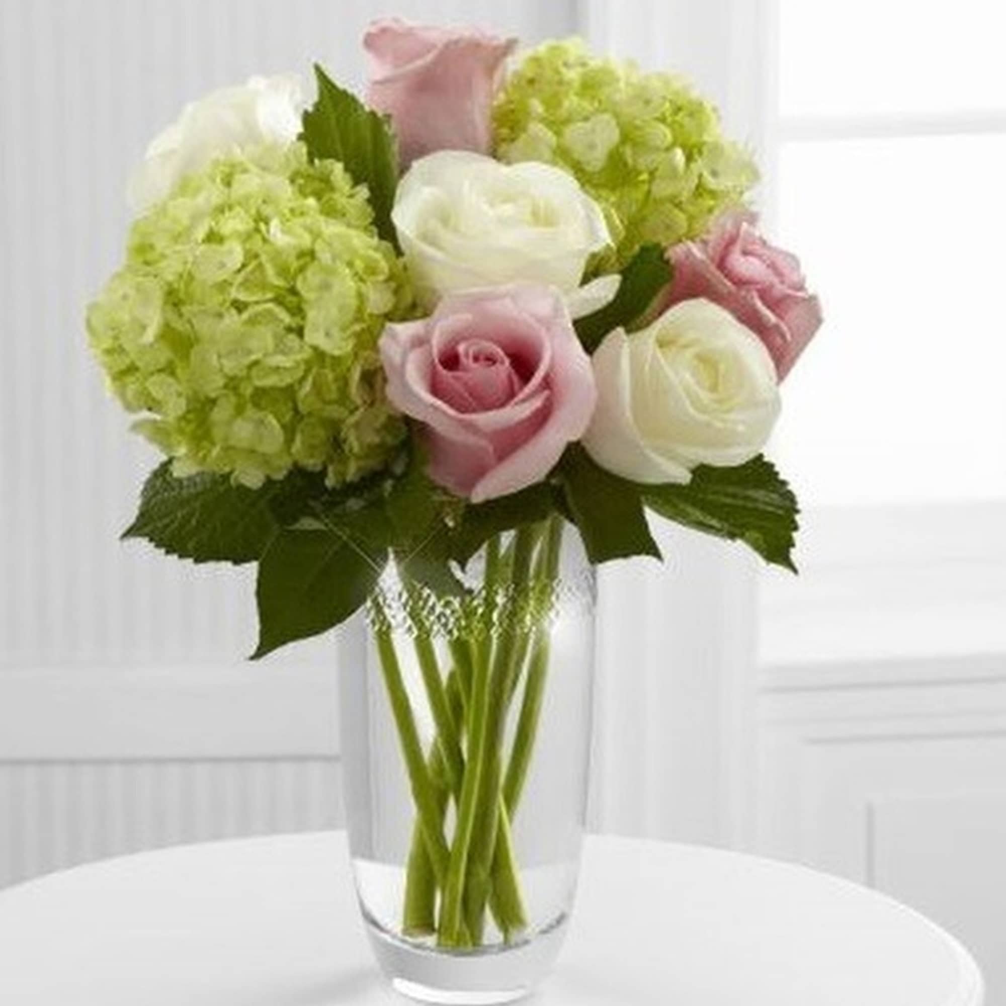 Arrangement of pale pink roses, white roses, and green hydrangeas in a clear glass vase