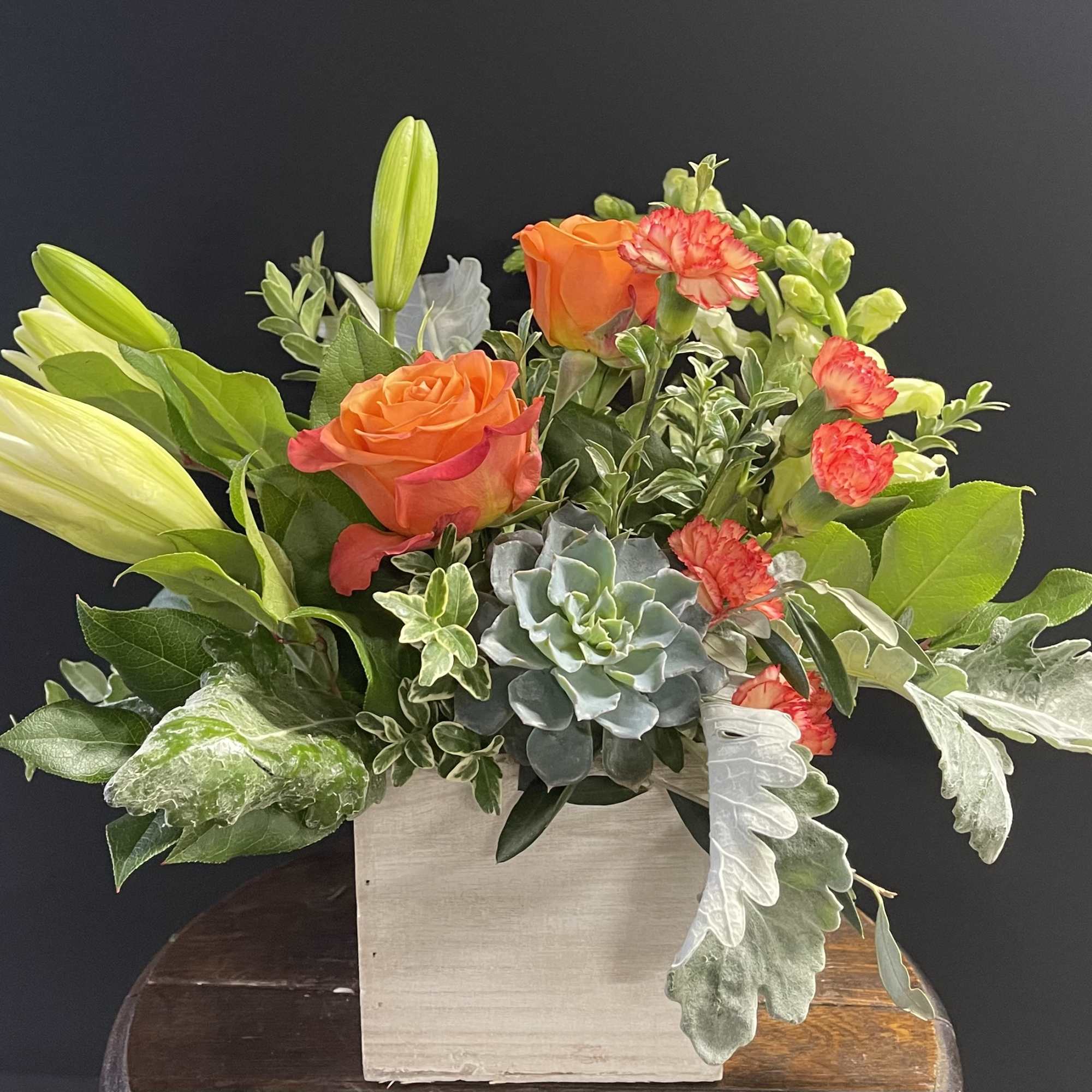 Orange roses and lilies in a square wooden container with succulents