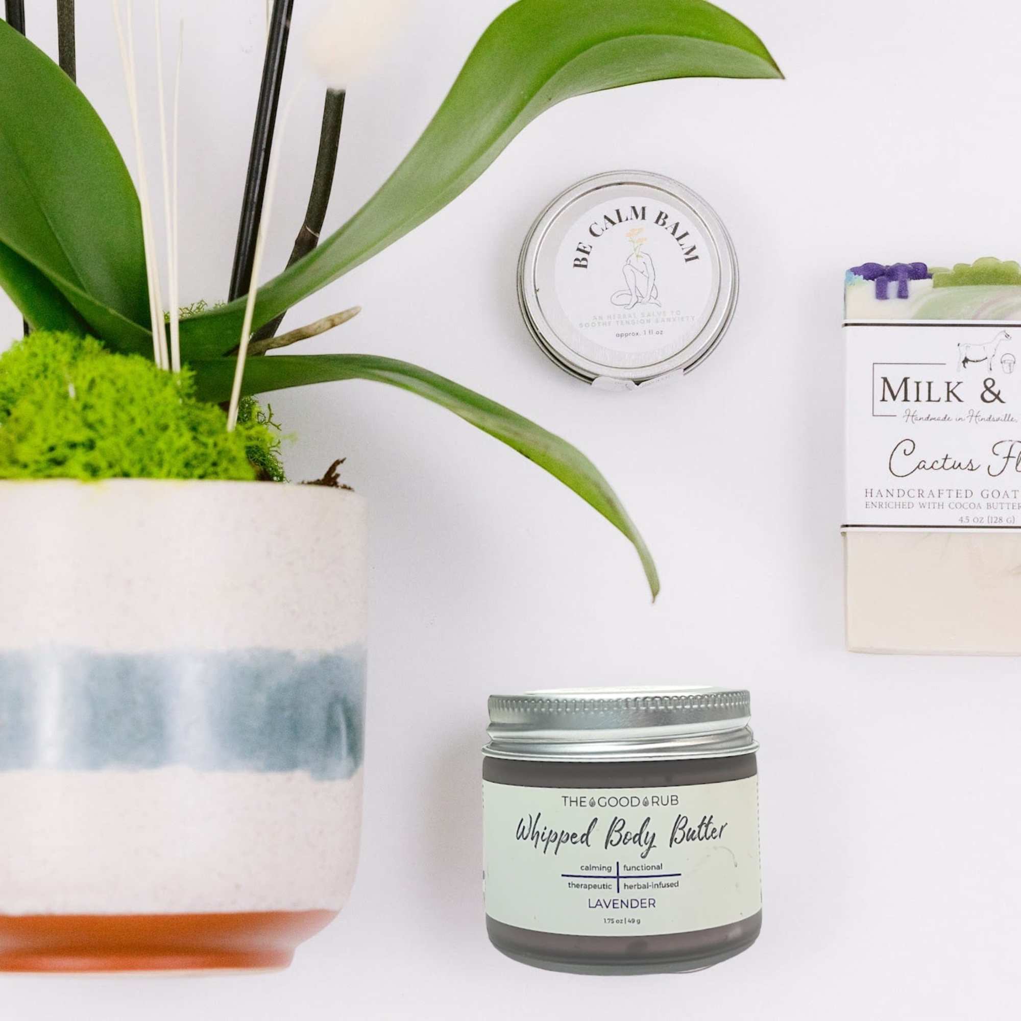 Potted orchid with a candle, soap bar, and body butter jars