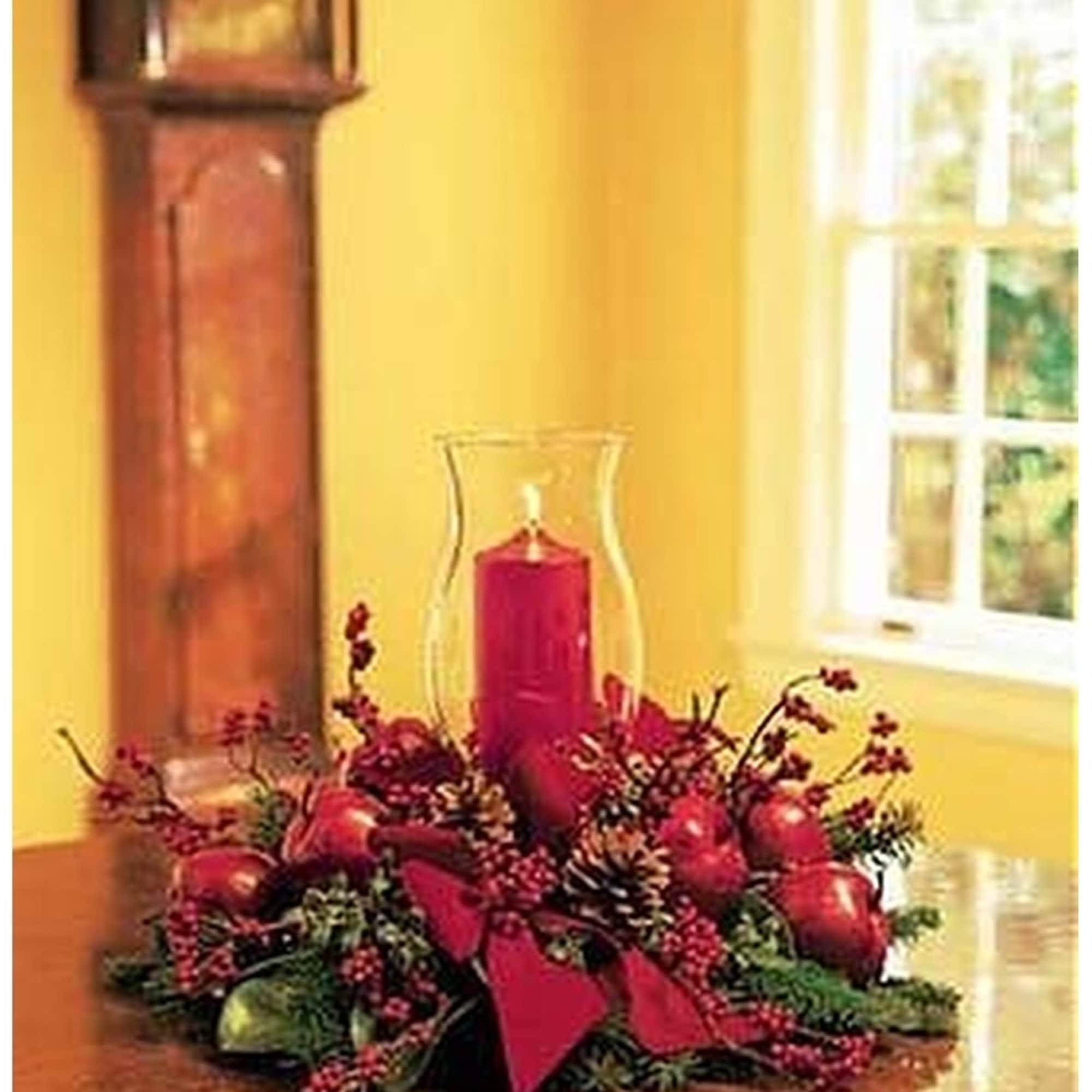 Red candle centerpiece with berries, apples, and pinecones on a table