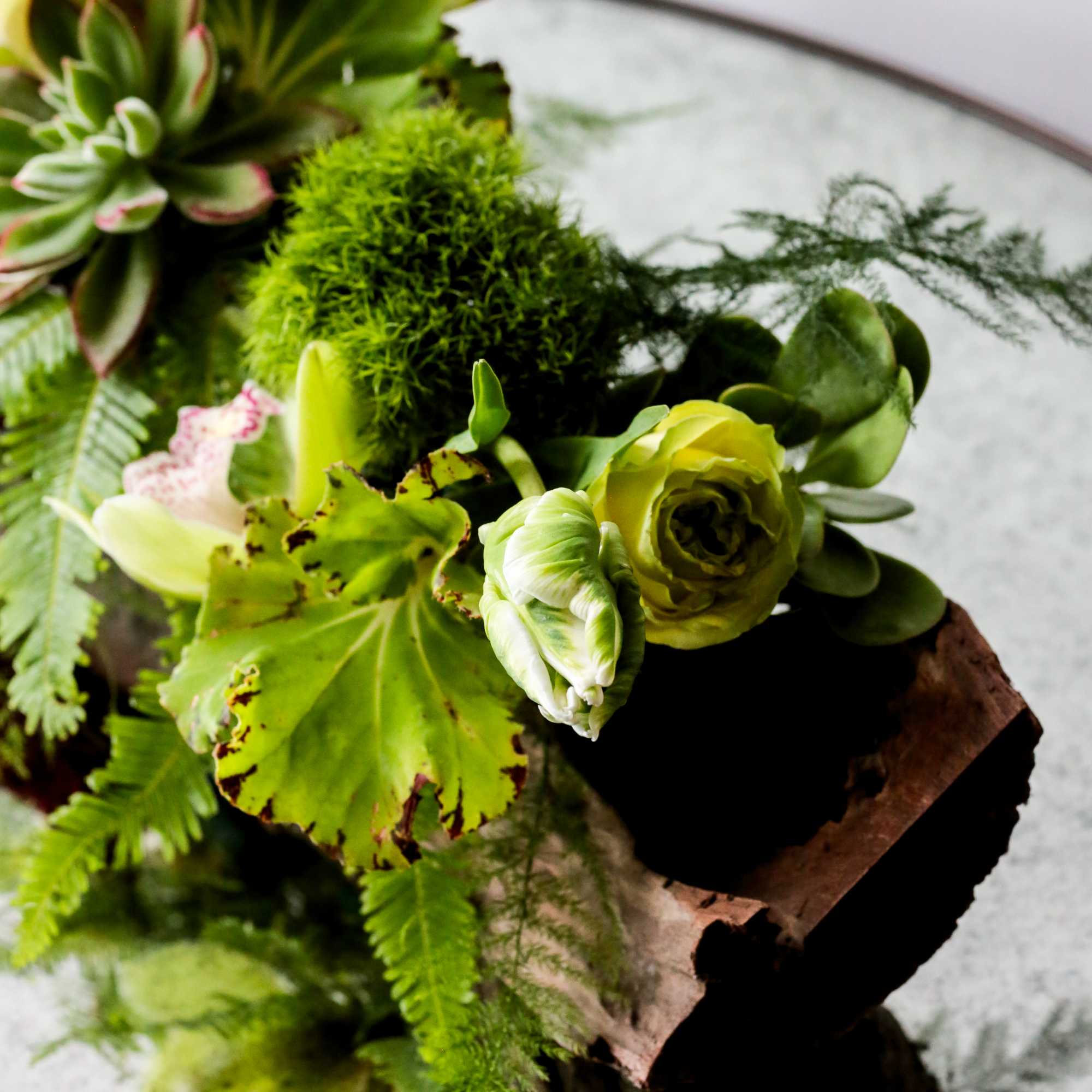 Green floral arrangement with succulents and pale blooms on wood