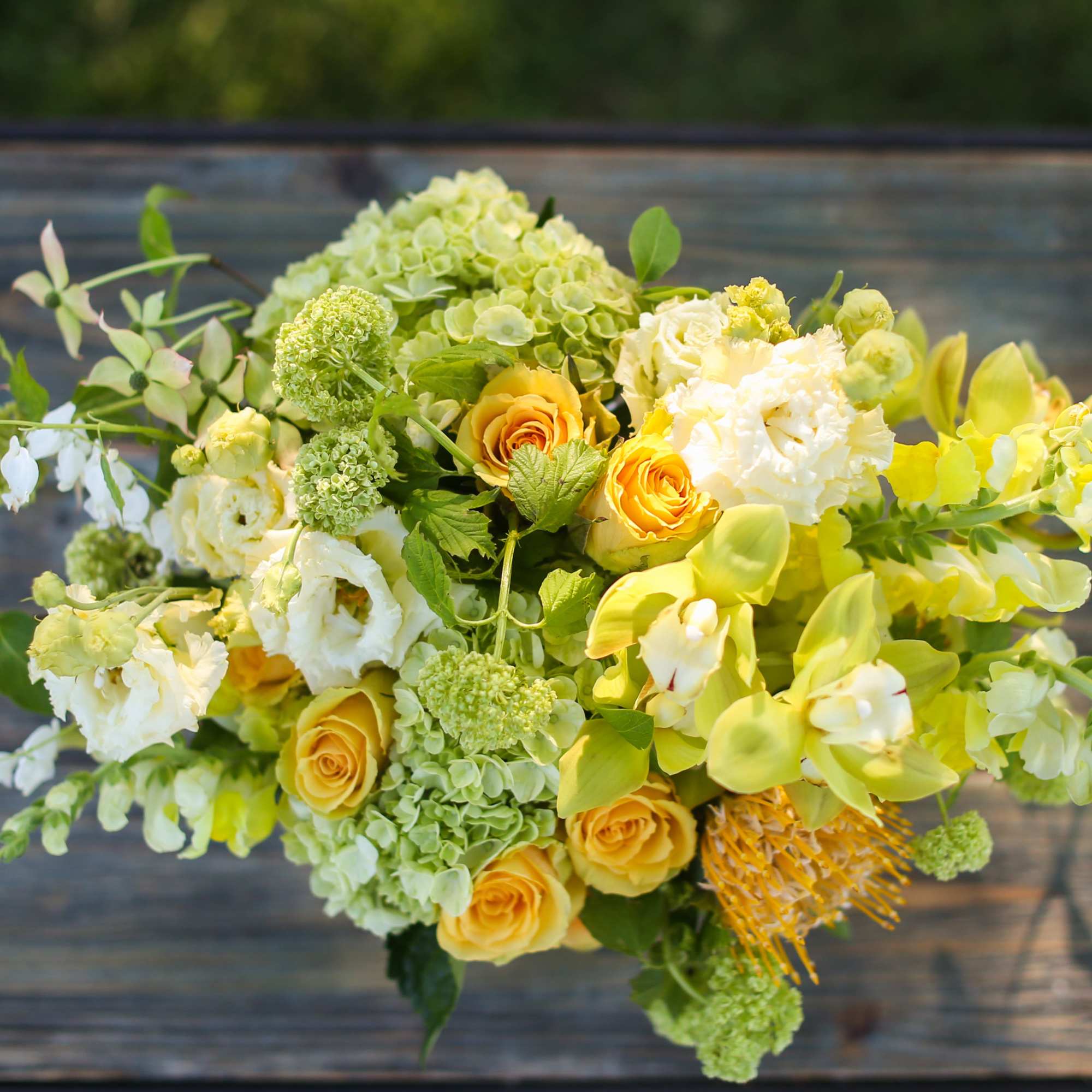 Bouquet of yellow and white flowers with green accents on a wooden surface