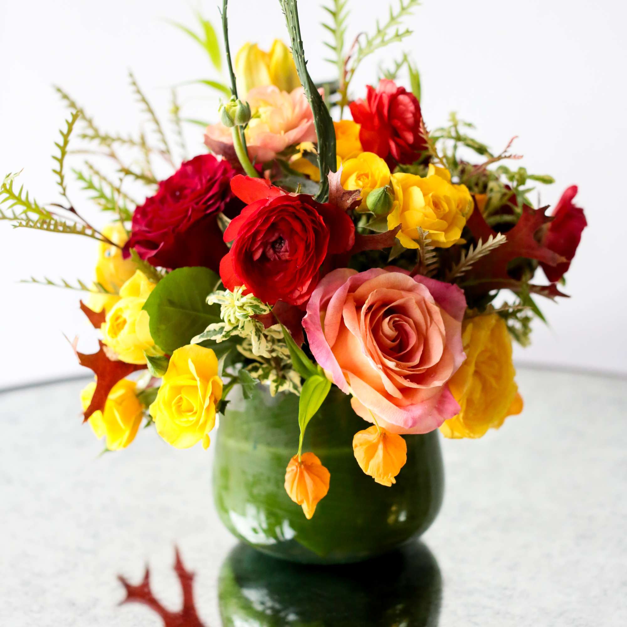 Mixed roses in a green glass vase with autumn leaves