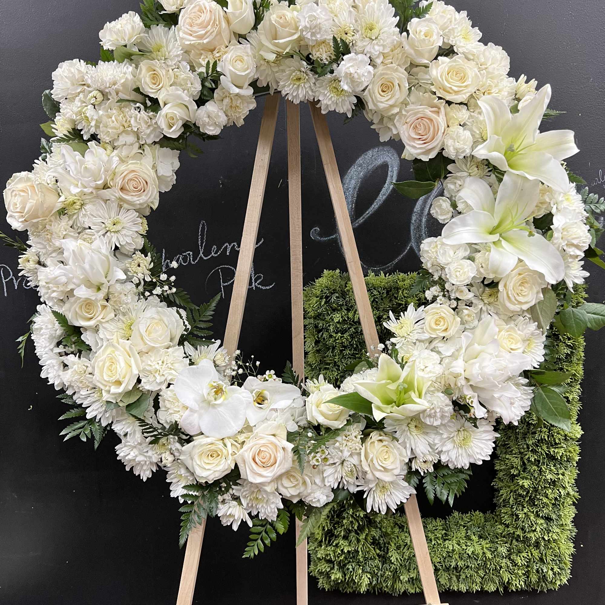 White floral wreath on a wooden easel with roses and lilies