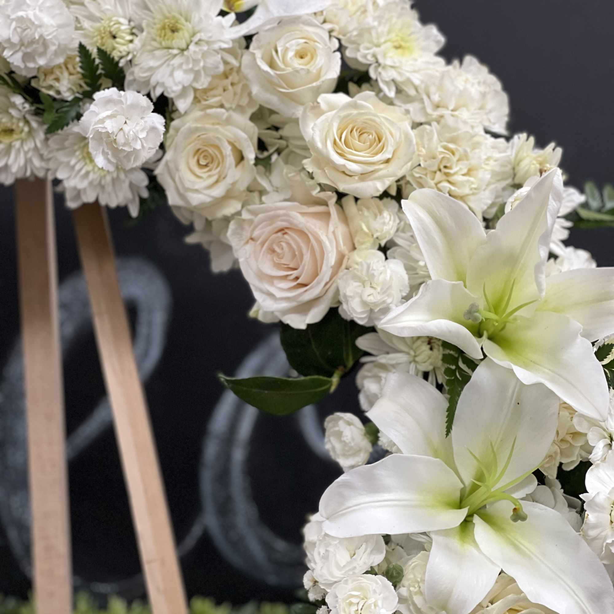 White floral arrangement with roses, lilies, and chrysanthemums on an easel