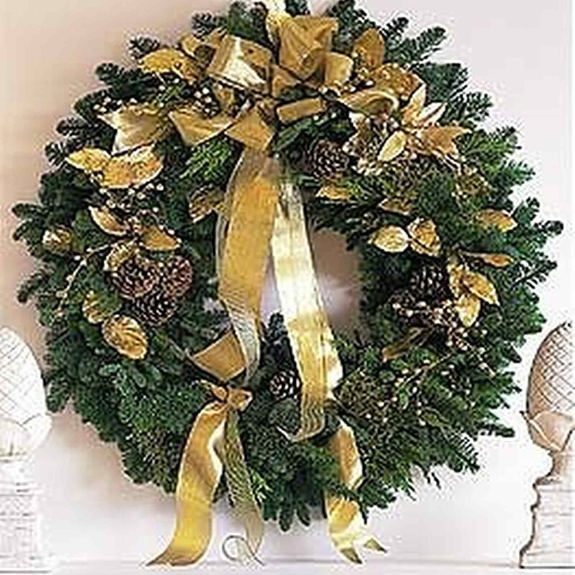 Evergreen wreath with gold ribbon, pinecones, and gold accents hanging above a mantel.