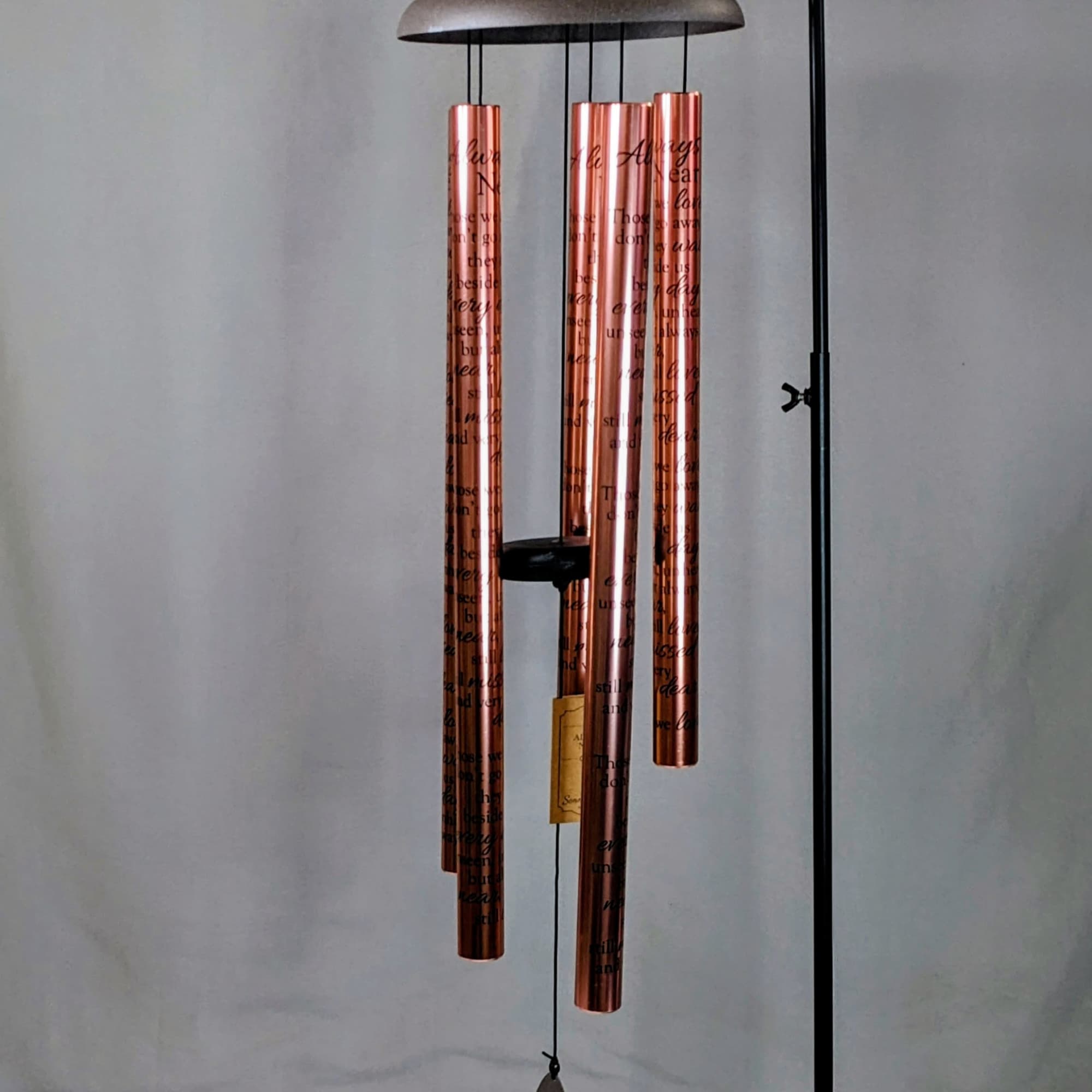 Copper wind chime hanging from a black metal stand