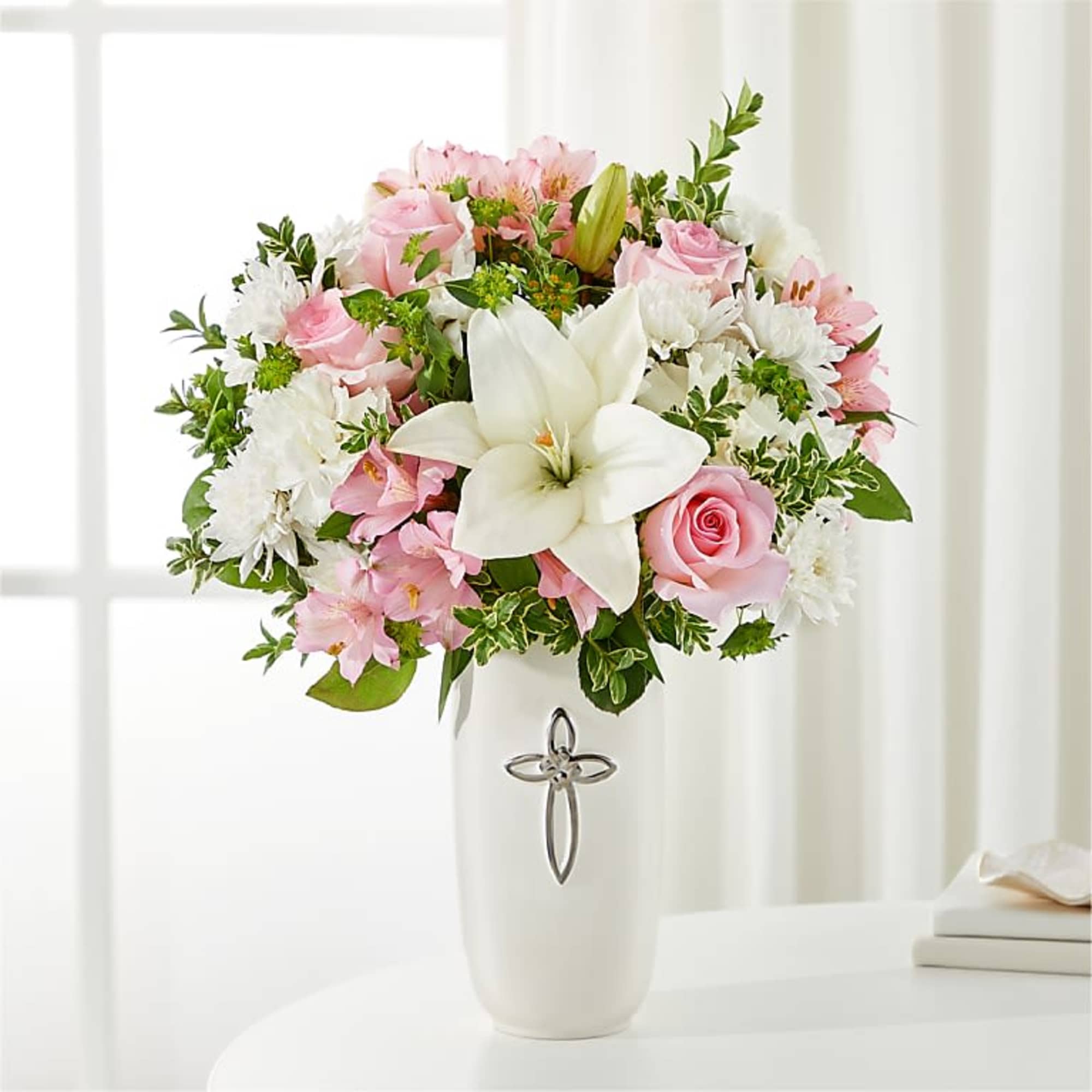 Pink and white flower arrangement in a white vase with a cross emblem