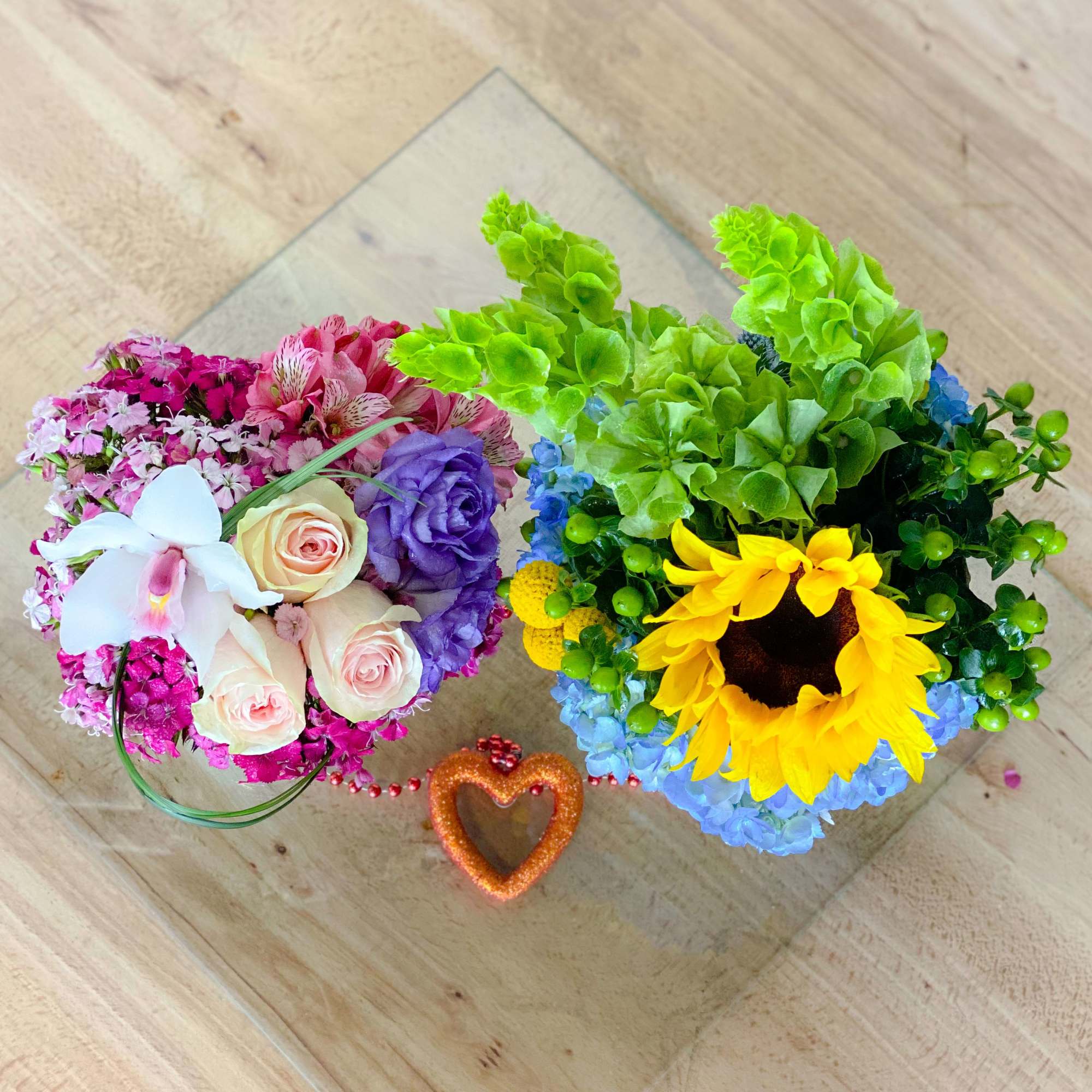 Two colorful floral arrangements on a glass tray with a small heart decoration